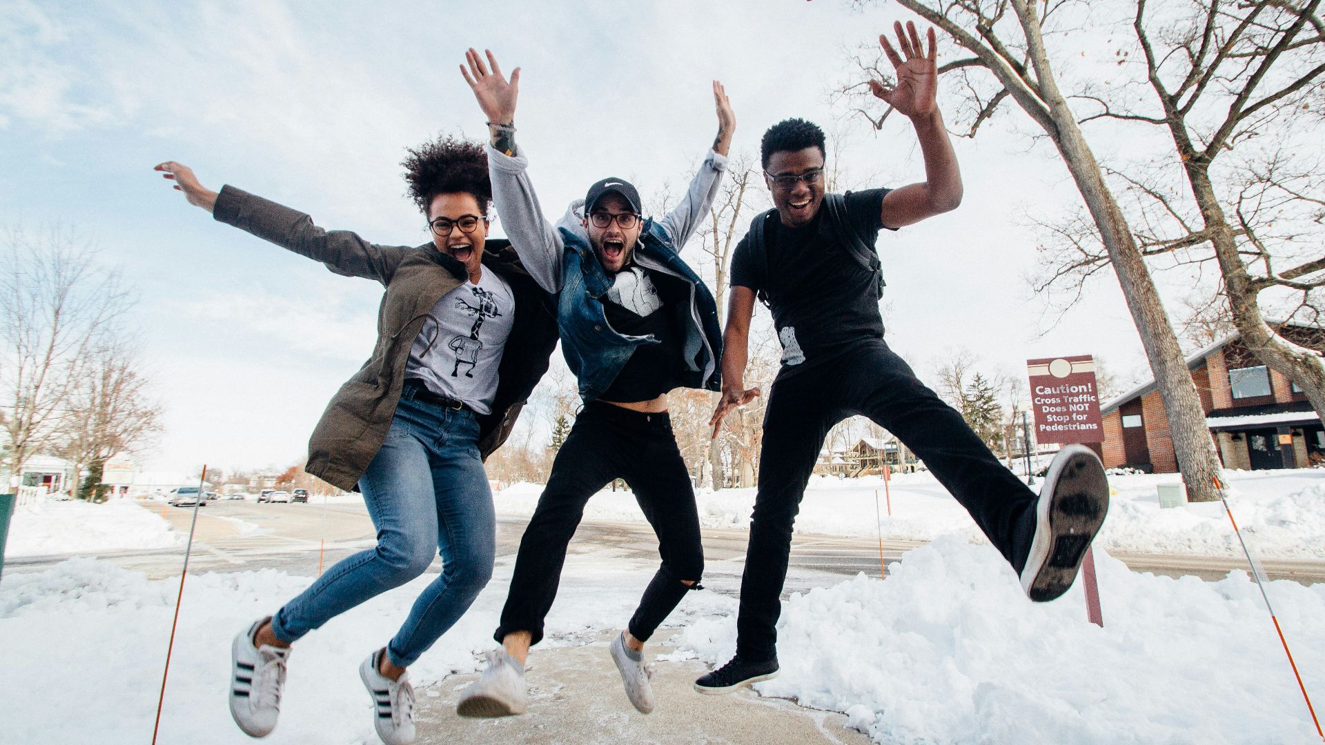 photo of three men jumping on ground near bare trees during daytime