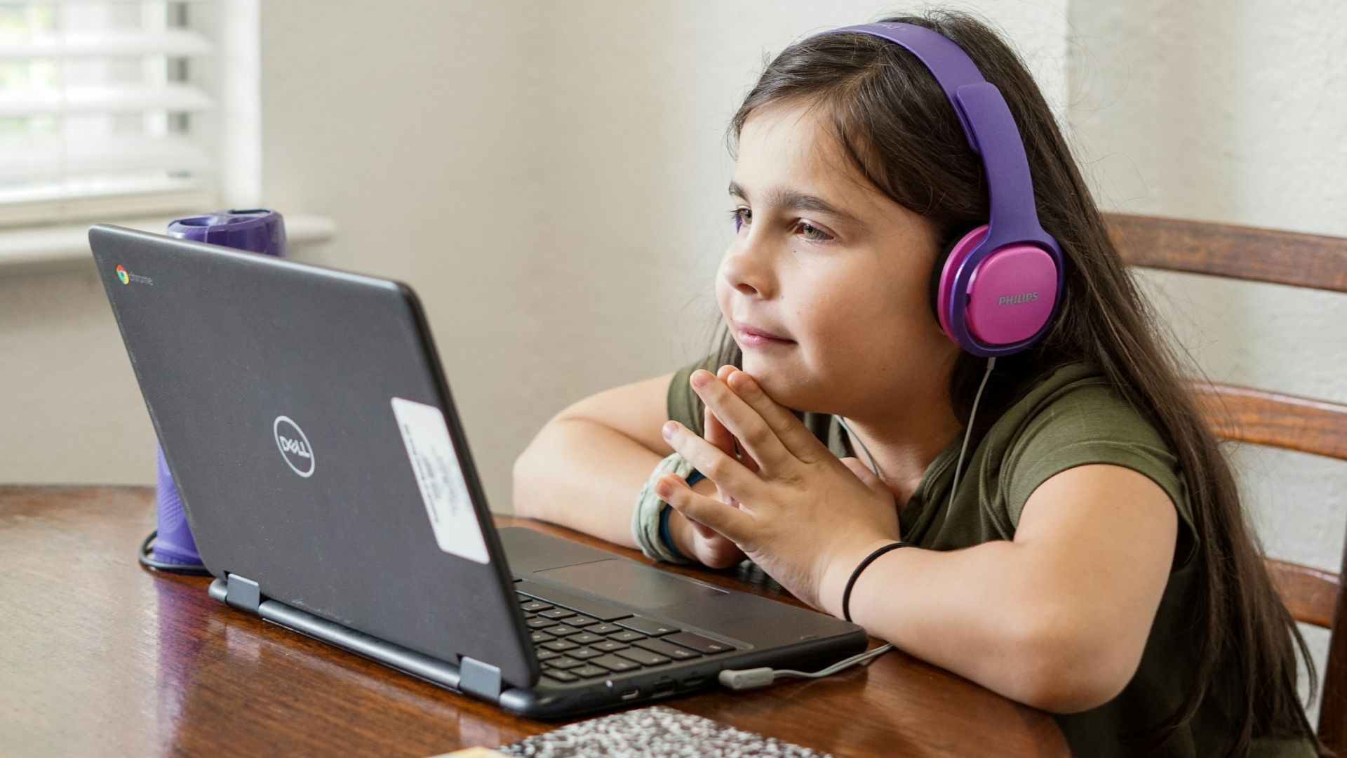 a little girl sitting at a table with a laptop