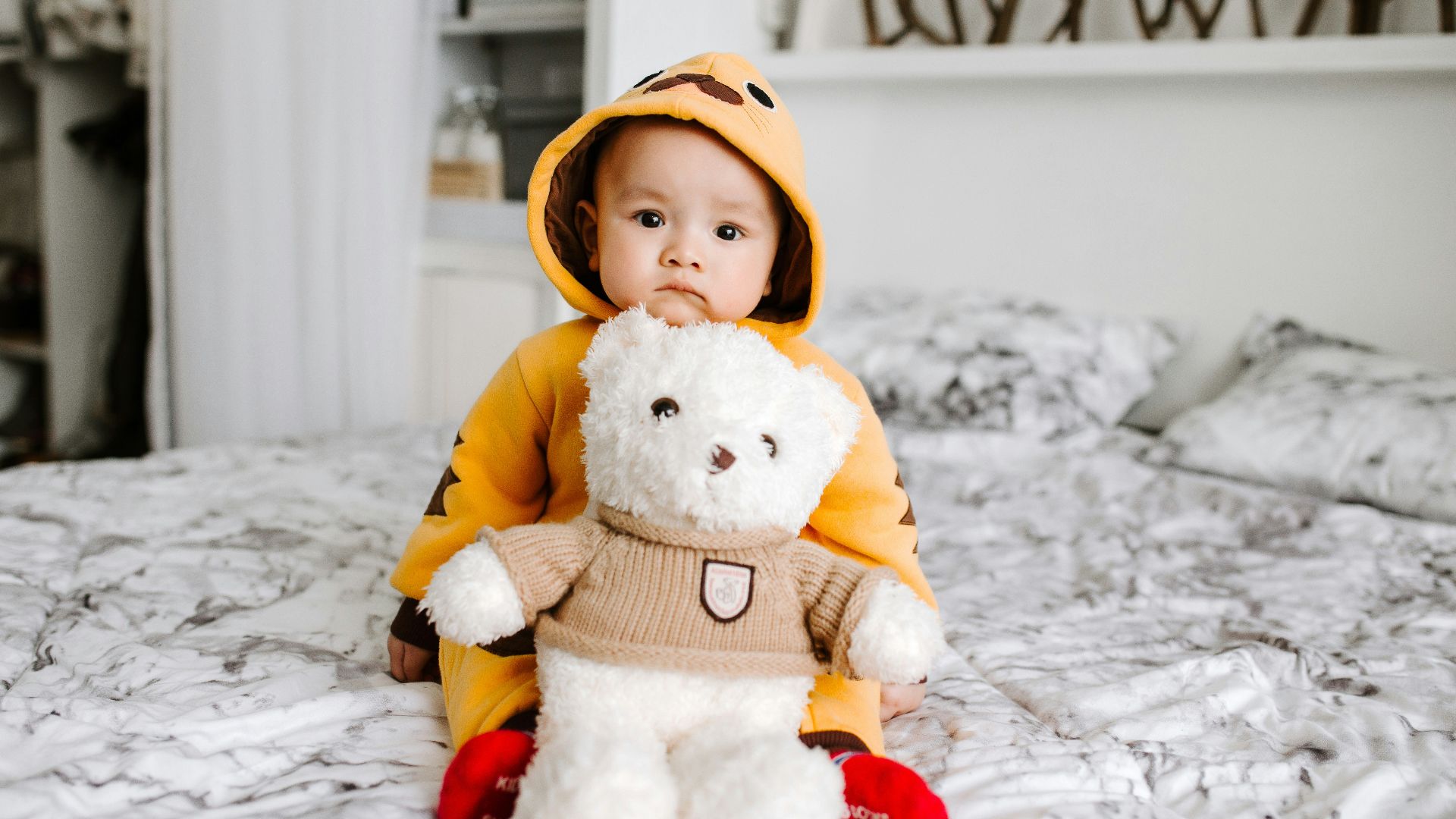 toddler sitting on bed beside white bear plush toy