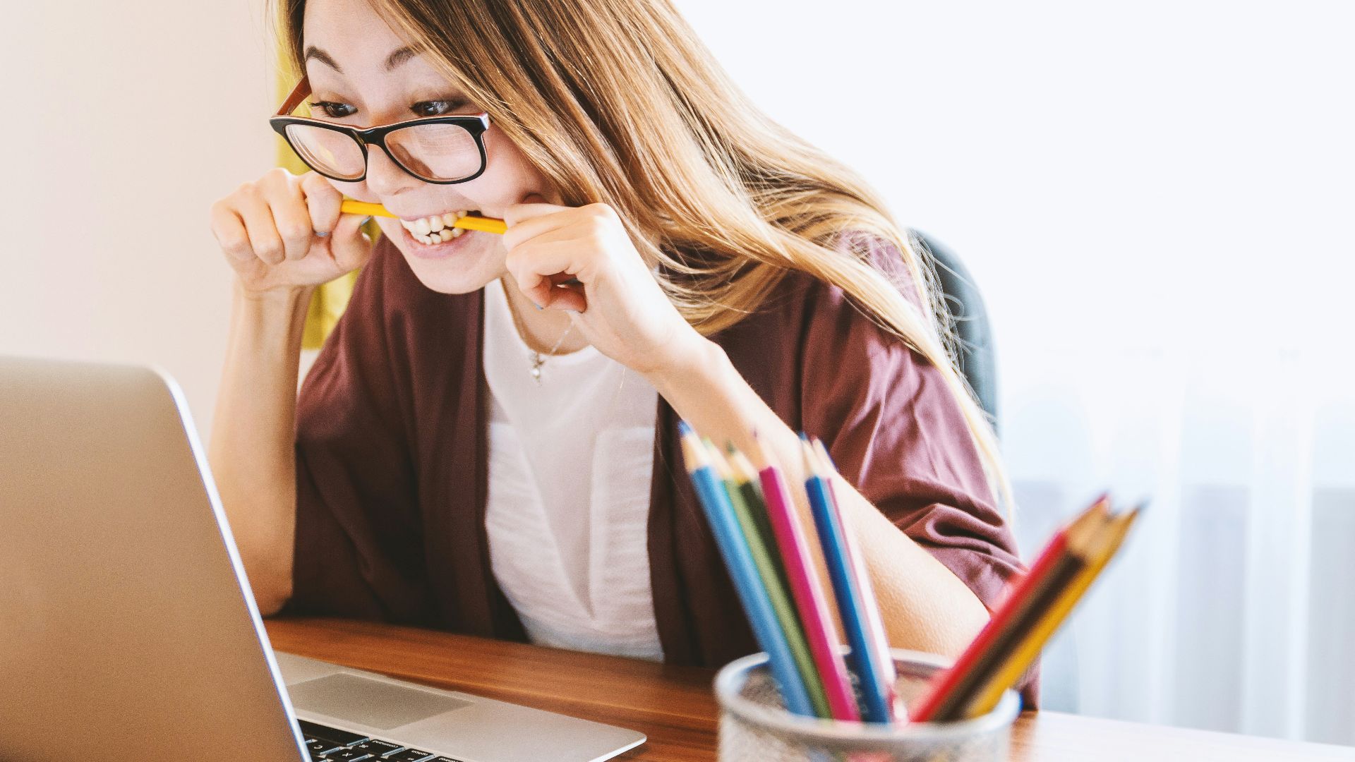 woman biting pencil while sitting on chair in front of computer during daytime