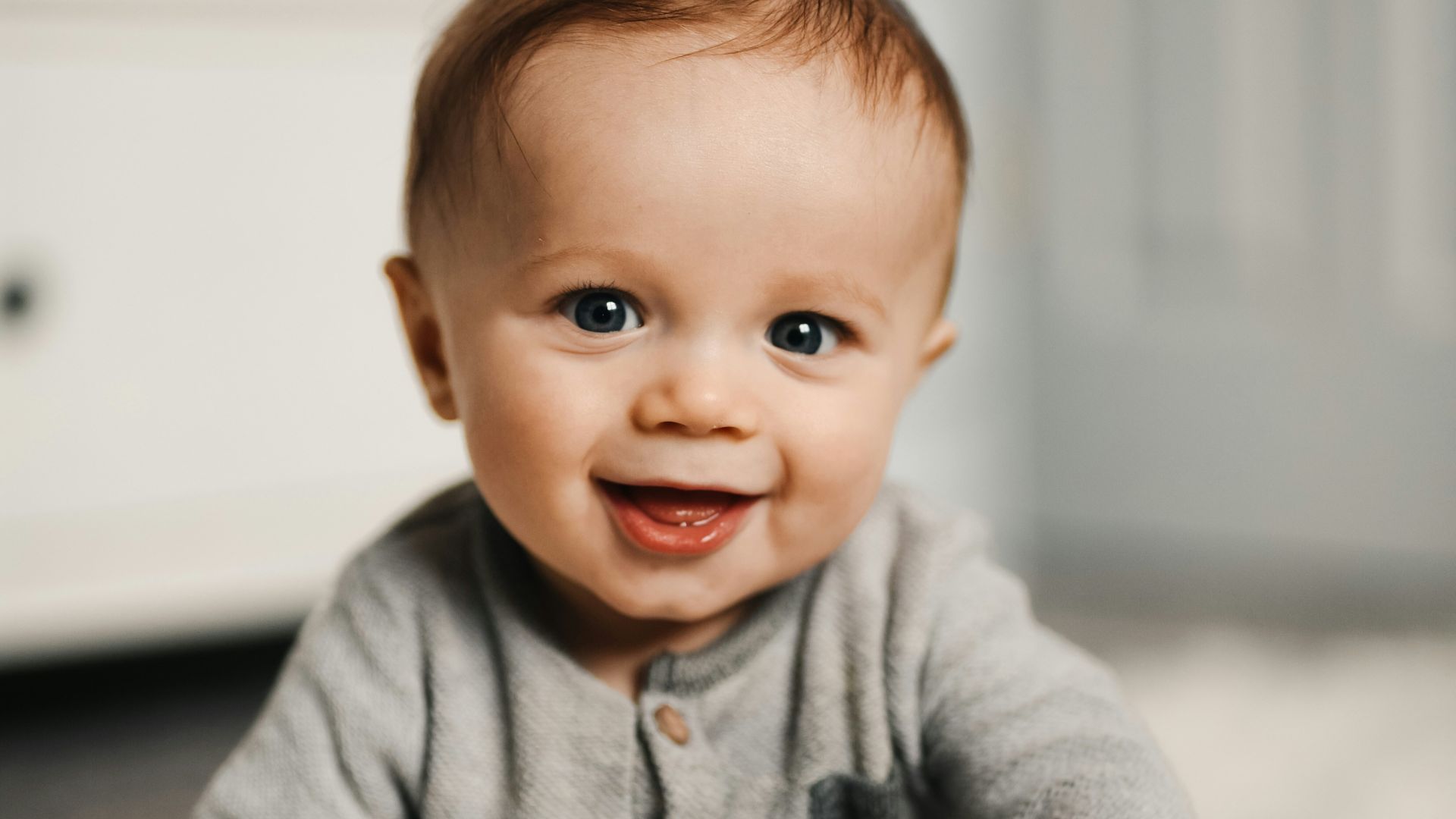 baby in gray sweater lying on white textile