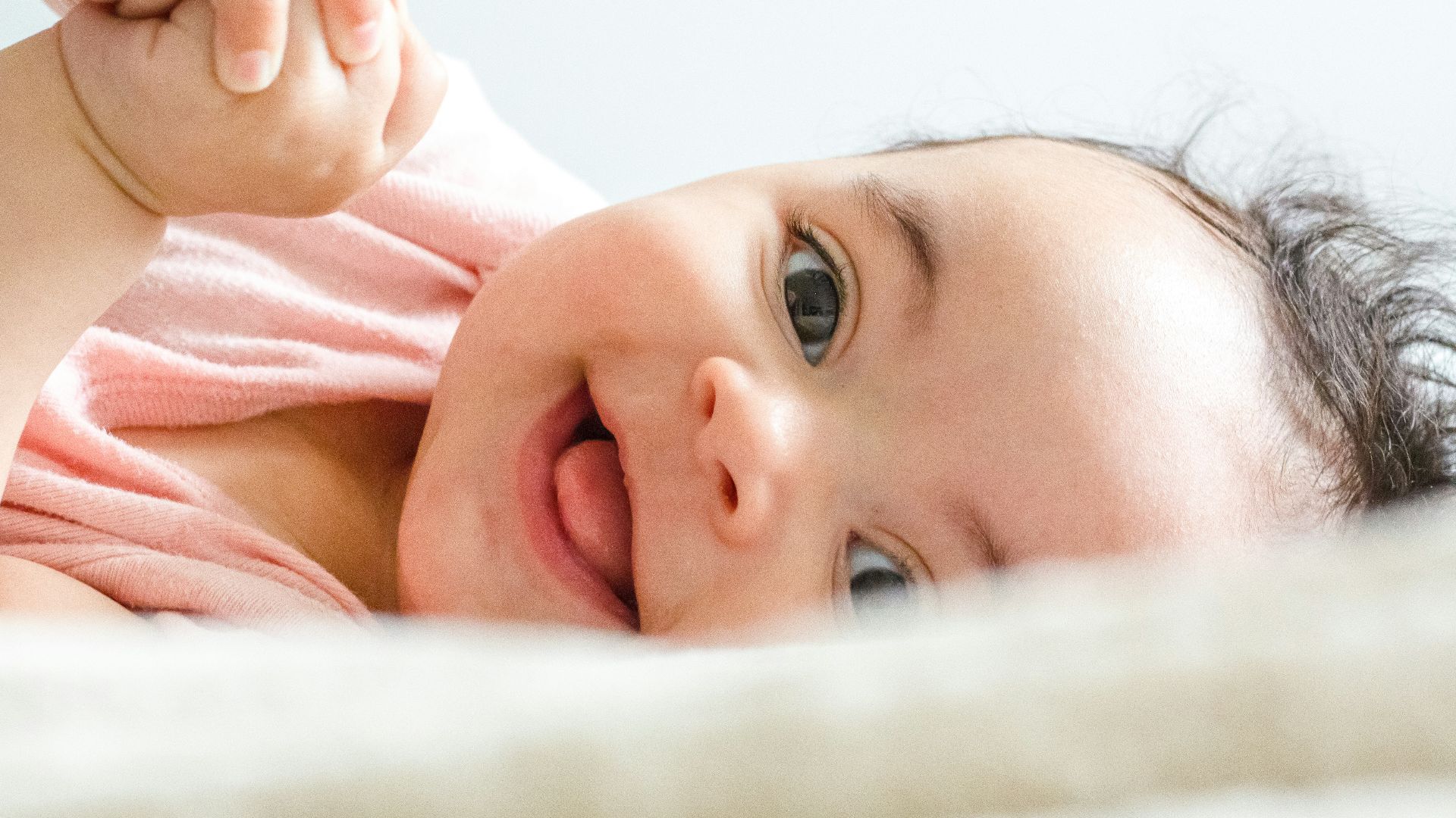 baby in pink shirt lying on white textile