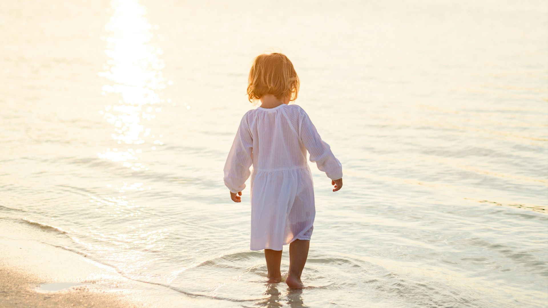 girl in white long sleeve shirt and white pants standing on beach during daytime
