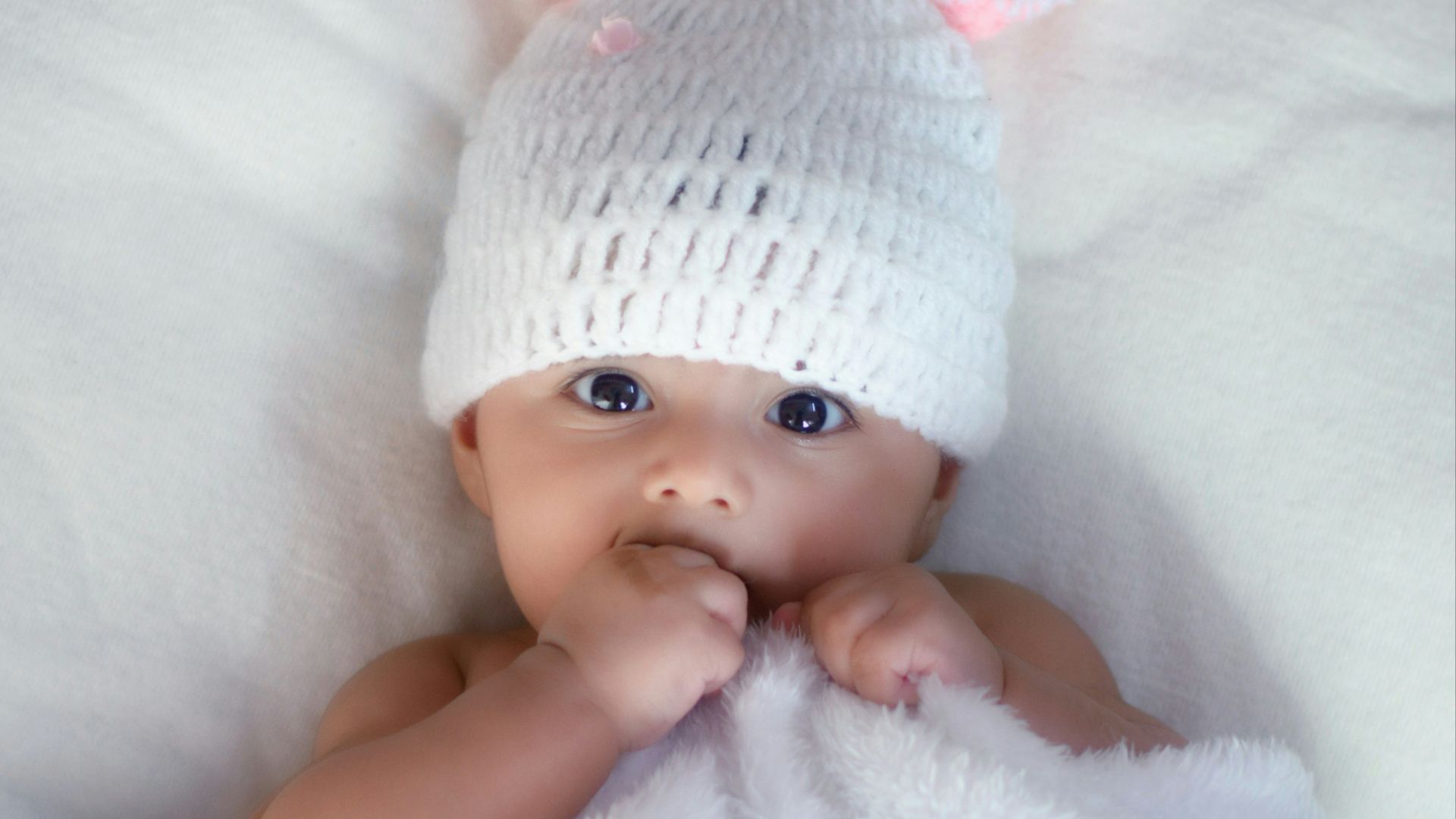 baby in white knit cap lying on white textile