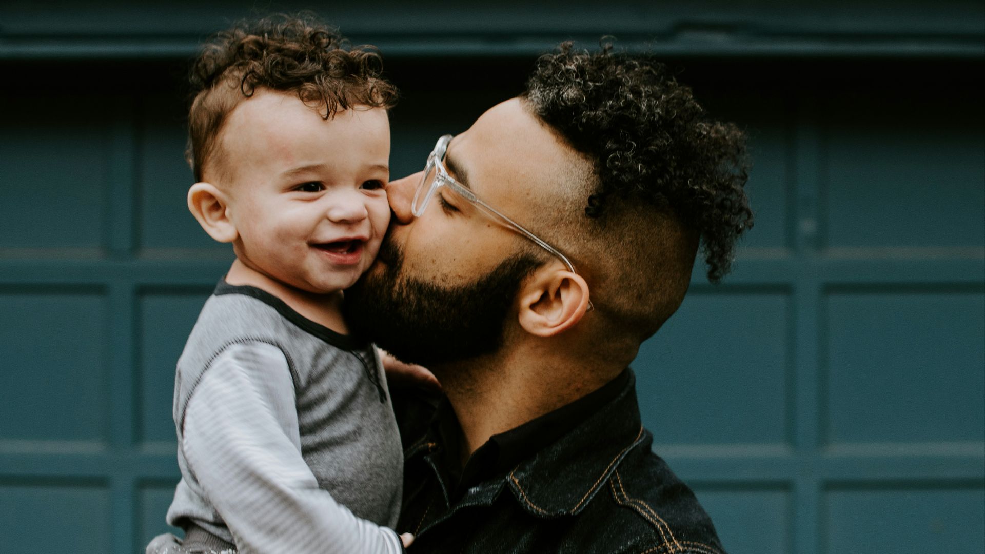 man carrying baby boy and kissing on cheek