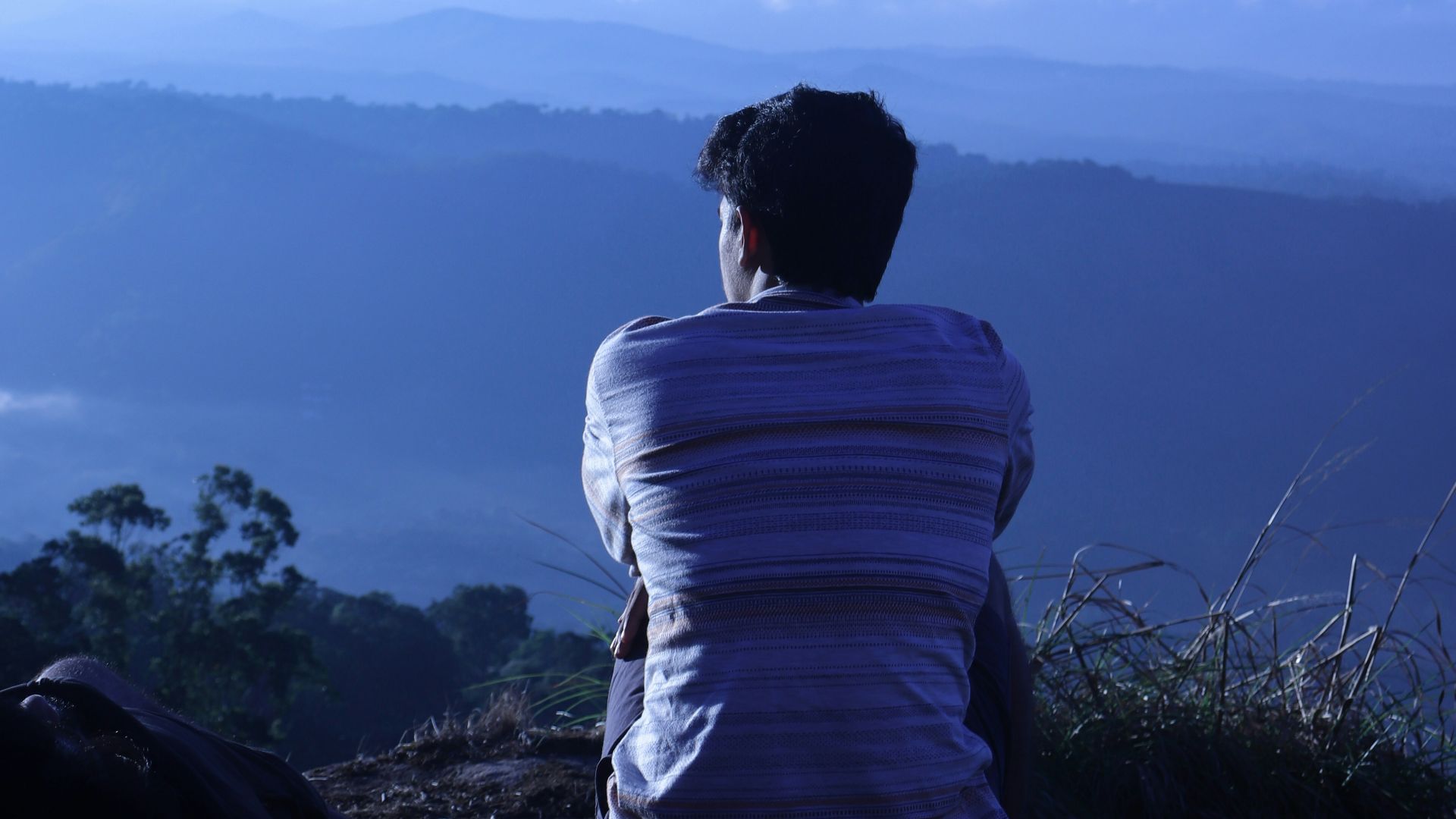 man in white shirt sitting on rock looking at mountains during daytime