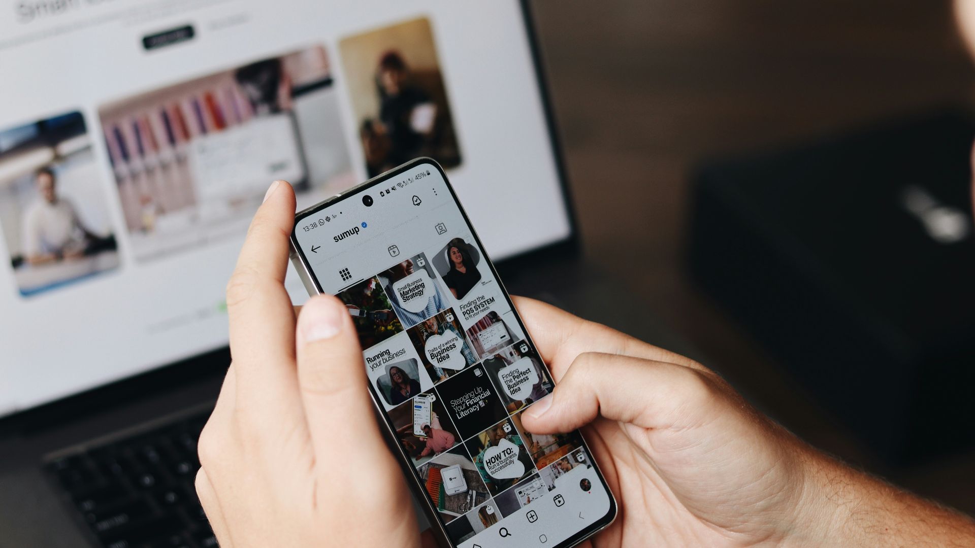 A person holding a cell phone in front of a laptop