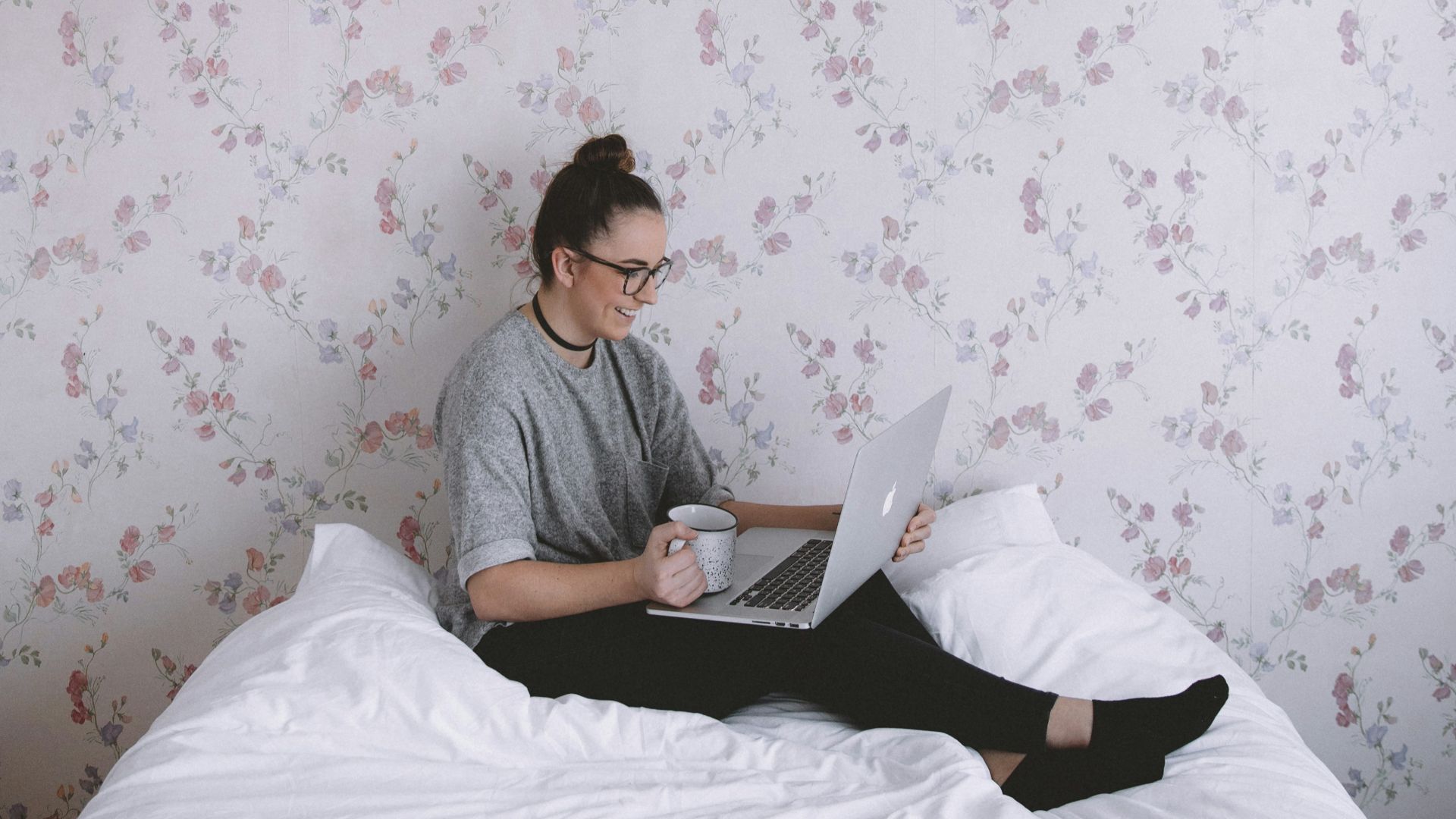 woman holding white ceramic cup while using laptop