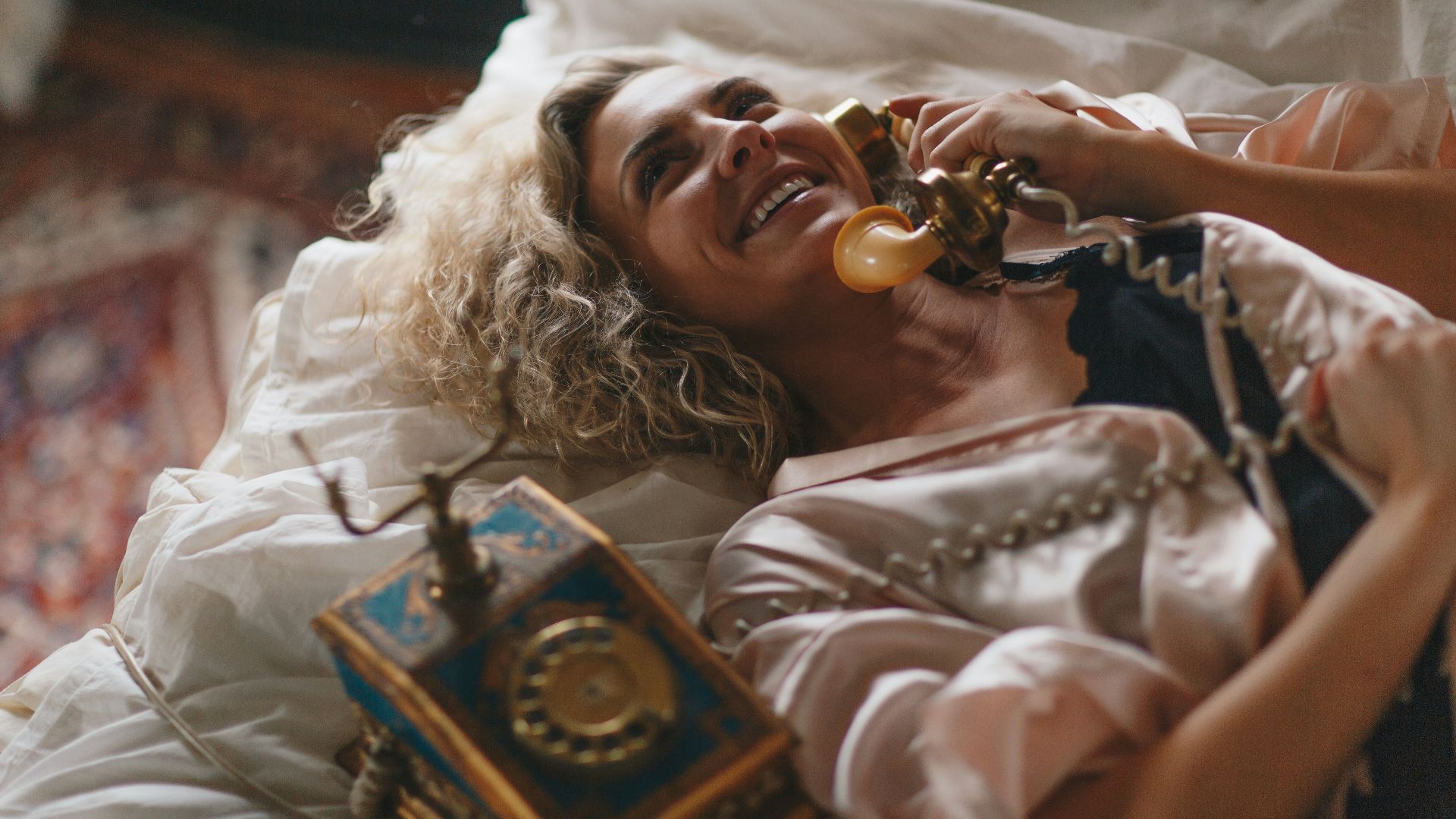 woman laying on white bed using a brown telephone