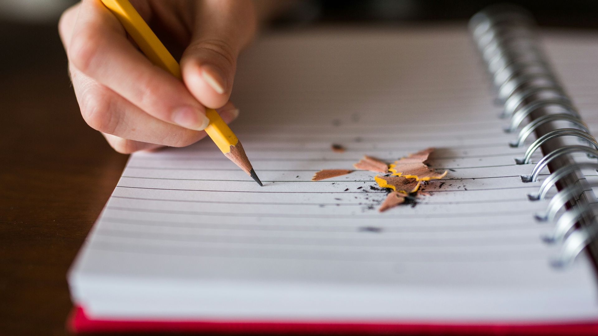 person holding pencil writing on notebook