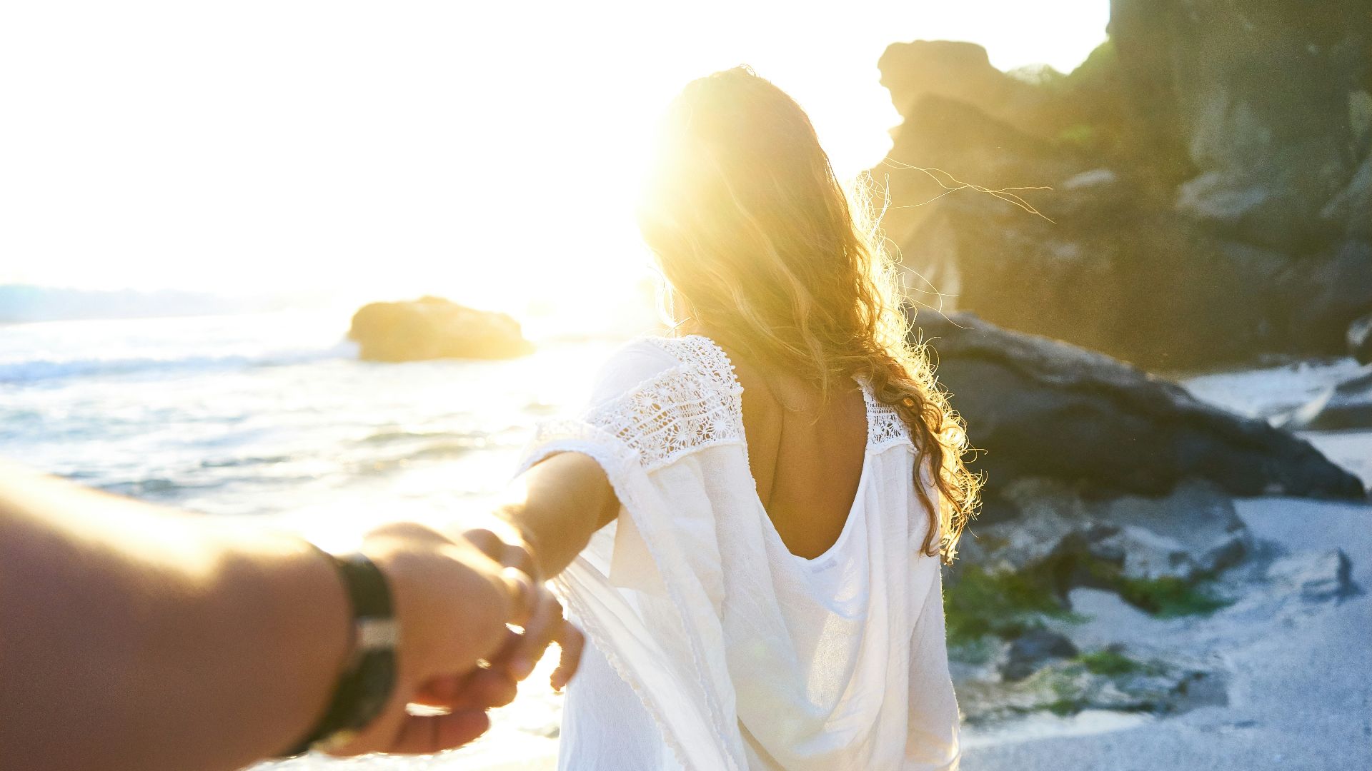person holding woman's hand beside sea while facing sunlight