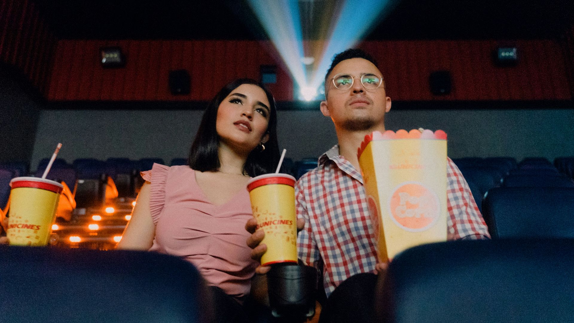 2 women sitting on blue leather chair holding white and red plastic cups