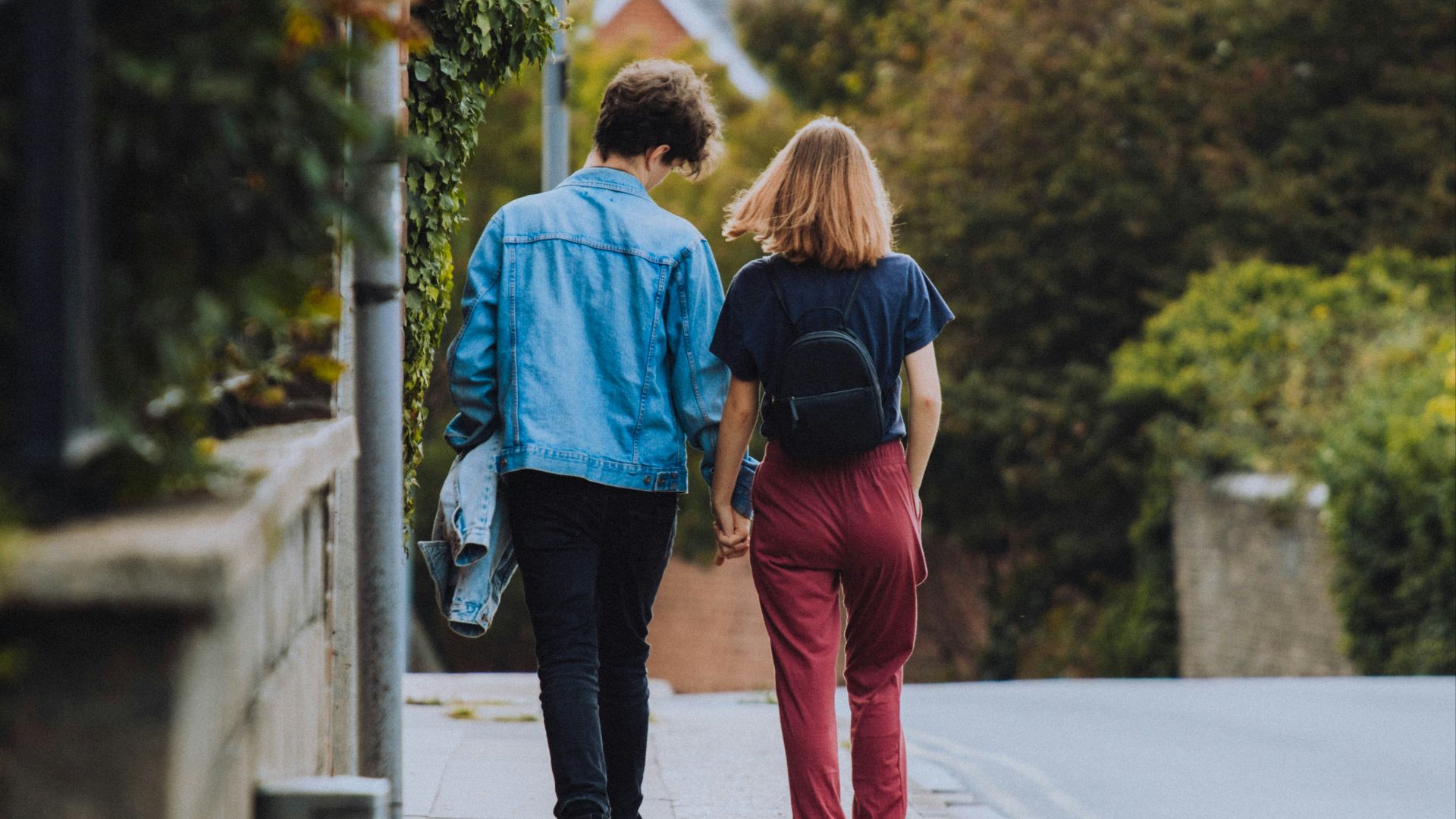 woman in blue jacket and red pants carrying black backpack walking on sidewalk during daytime