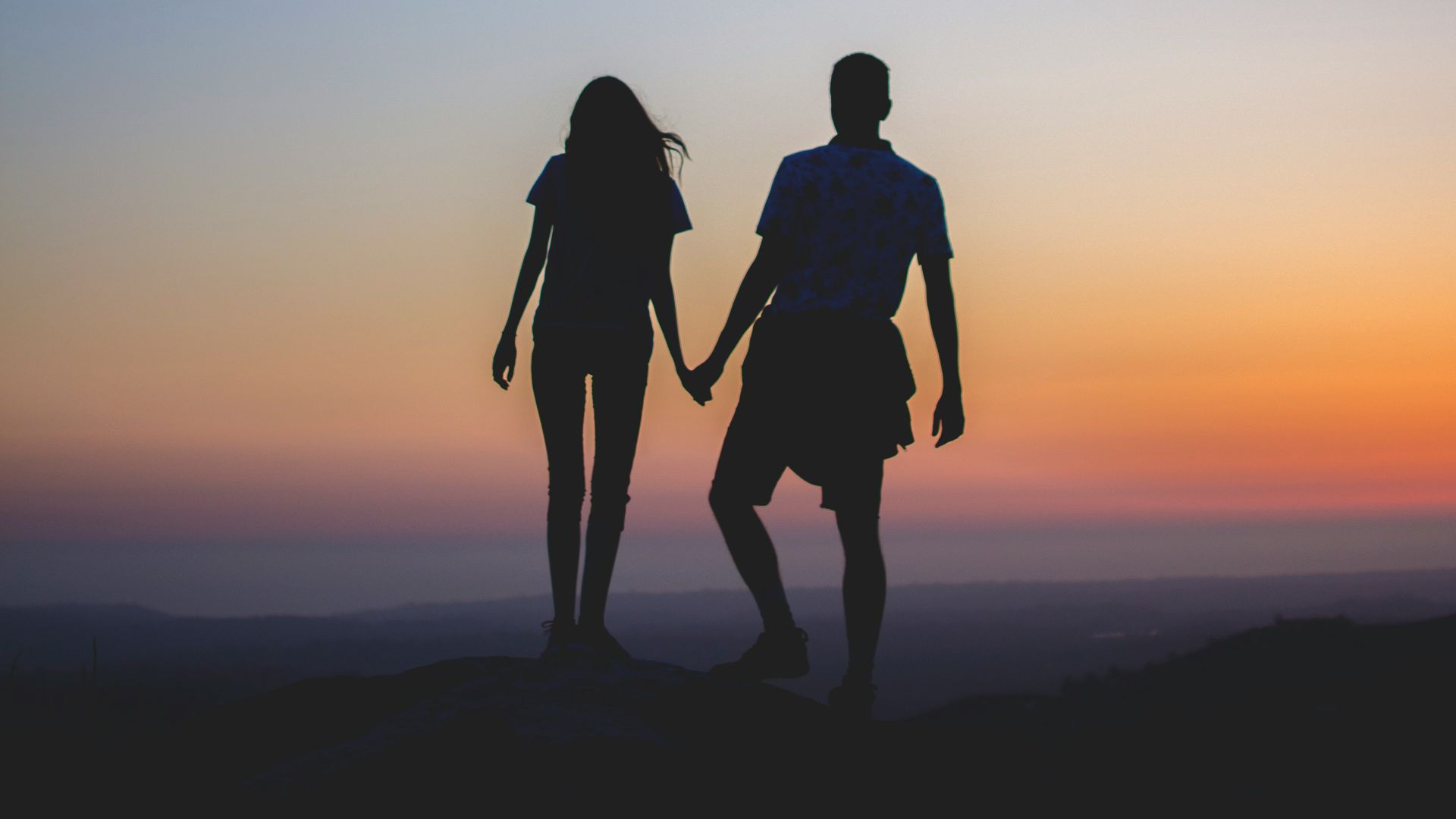man and woman holding hands in silhouette photography