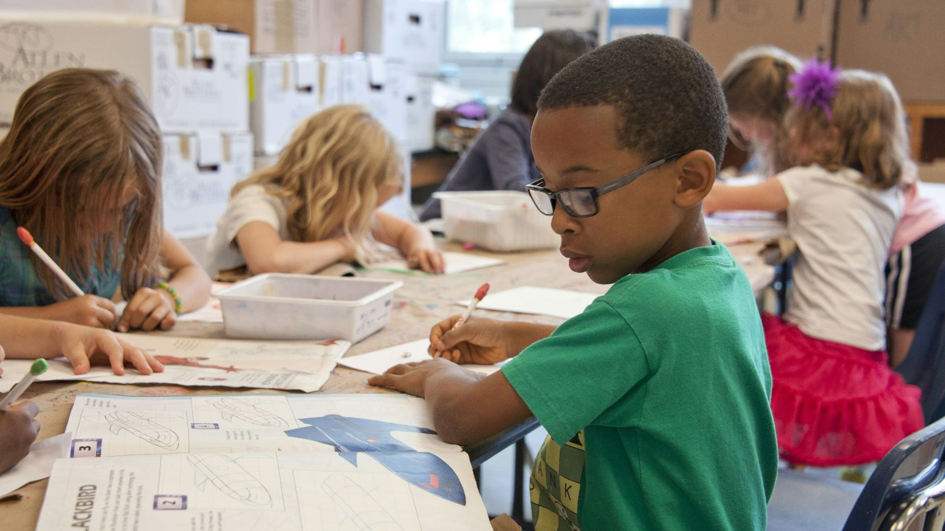 boy in green sweater writing on white paper