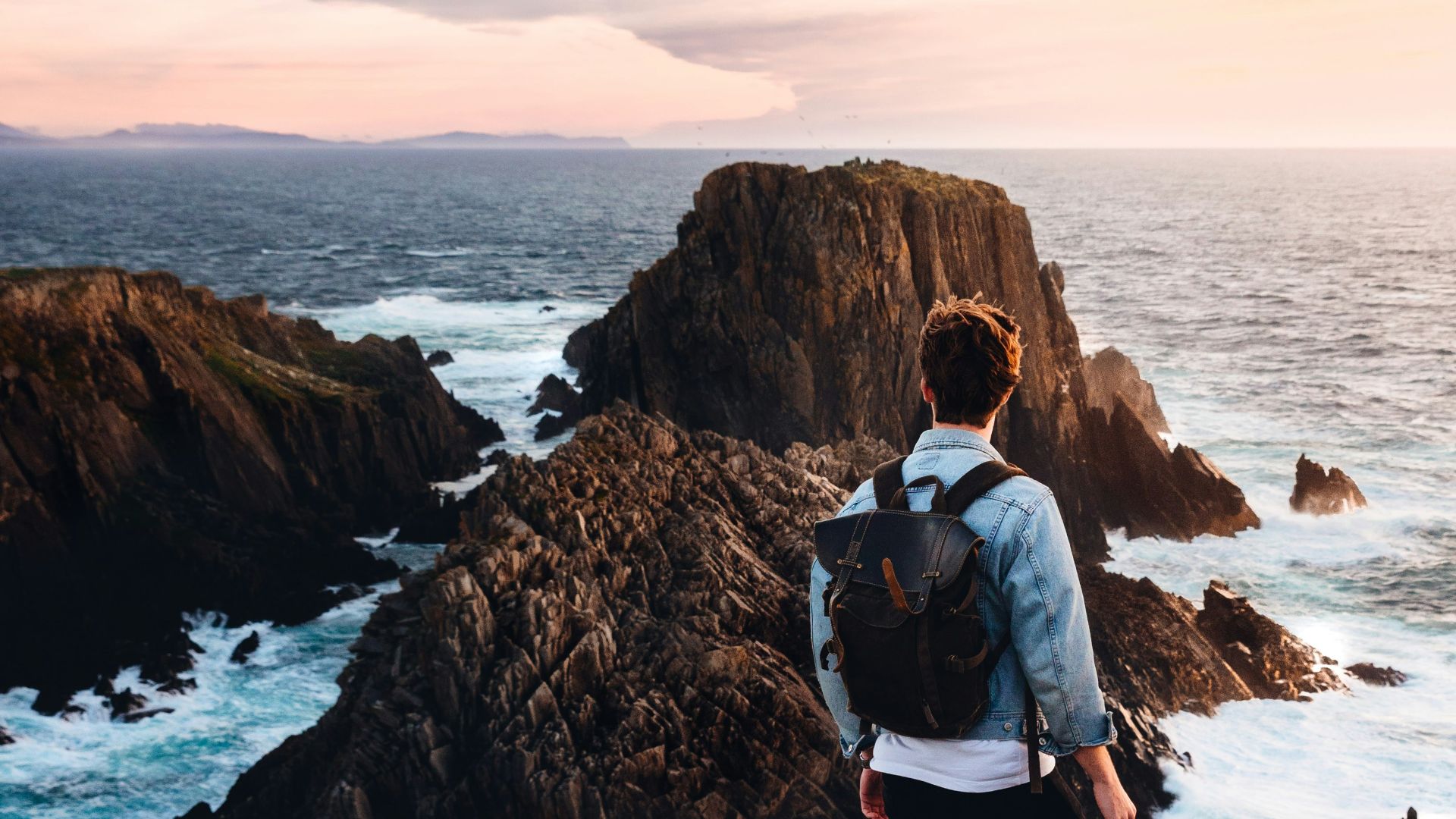 man standing near cliff looking at body of water during daytime