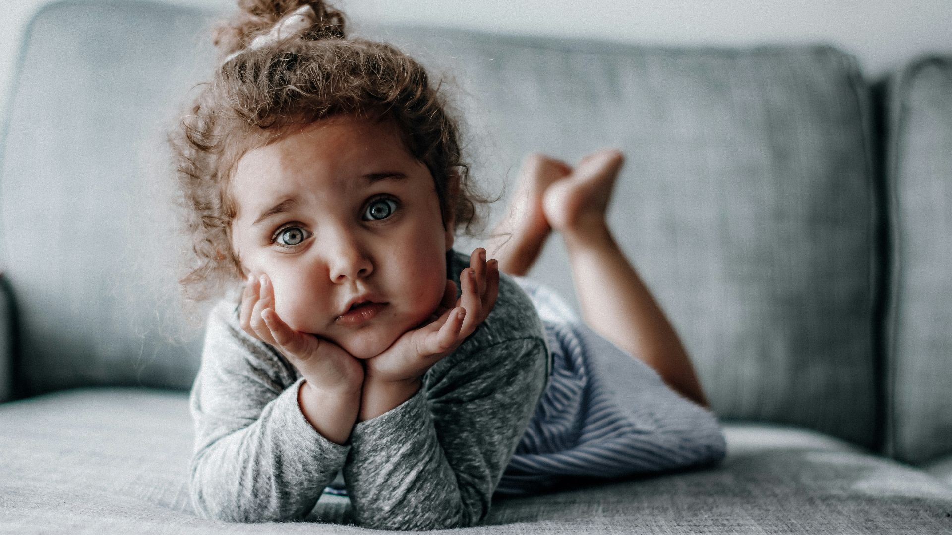 girl in gray long sleeve shirt lying on gray textile
