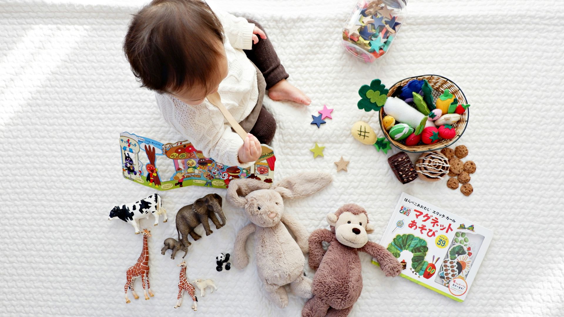 boy sitting on white cloth surrounded by toys