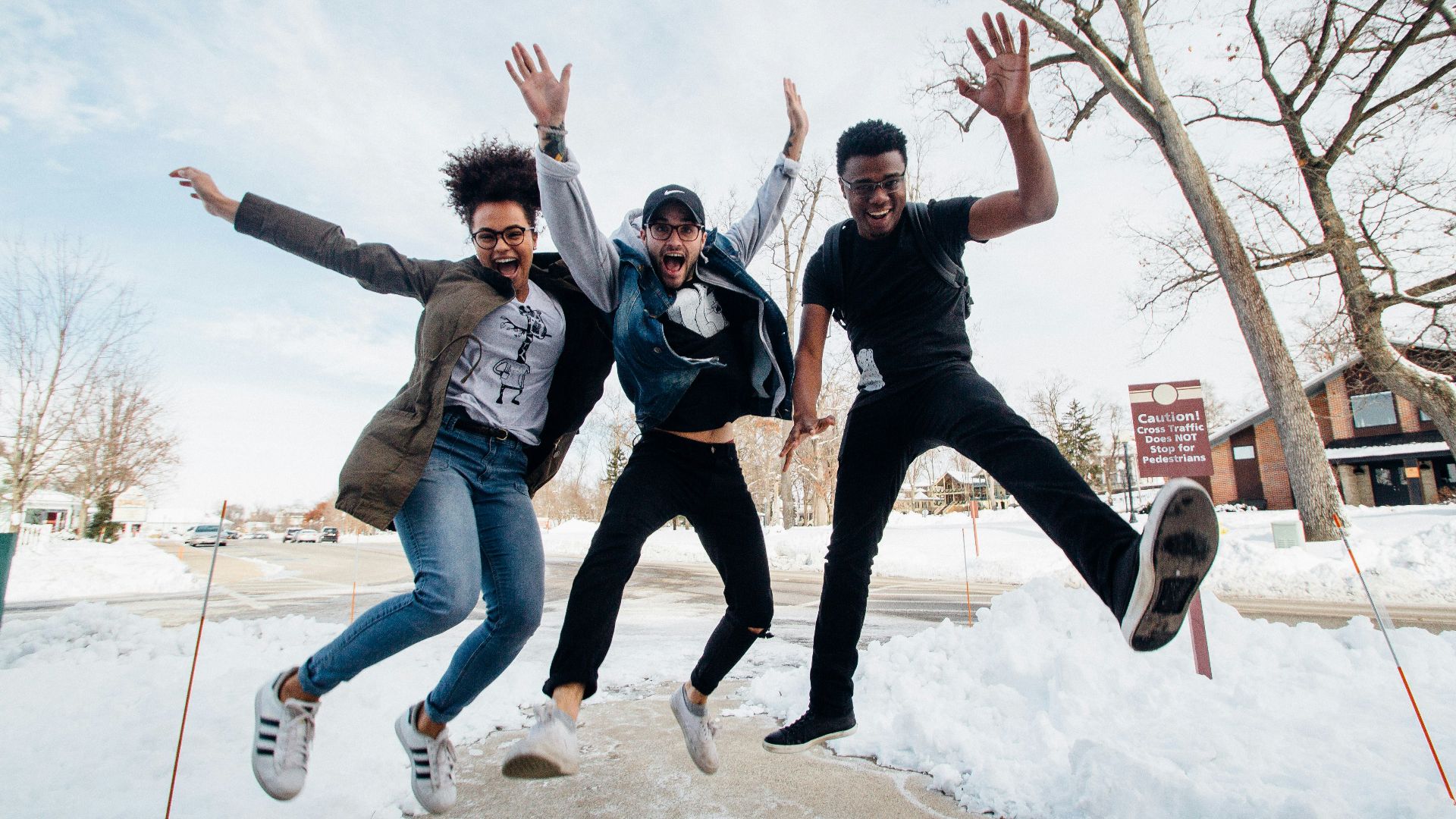 photo of three men jumping on ground near bare trees during daytime