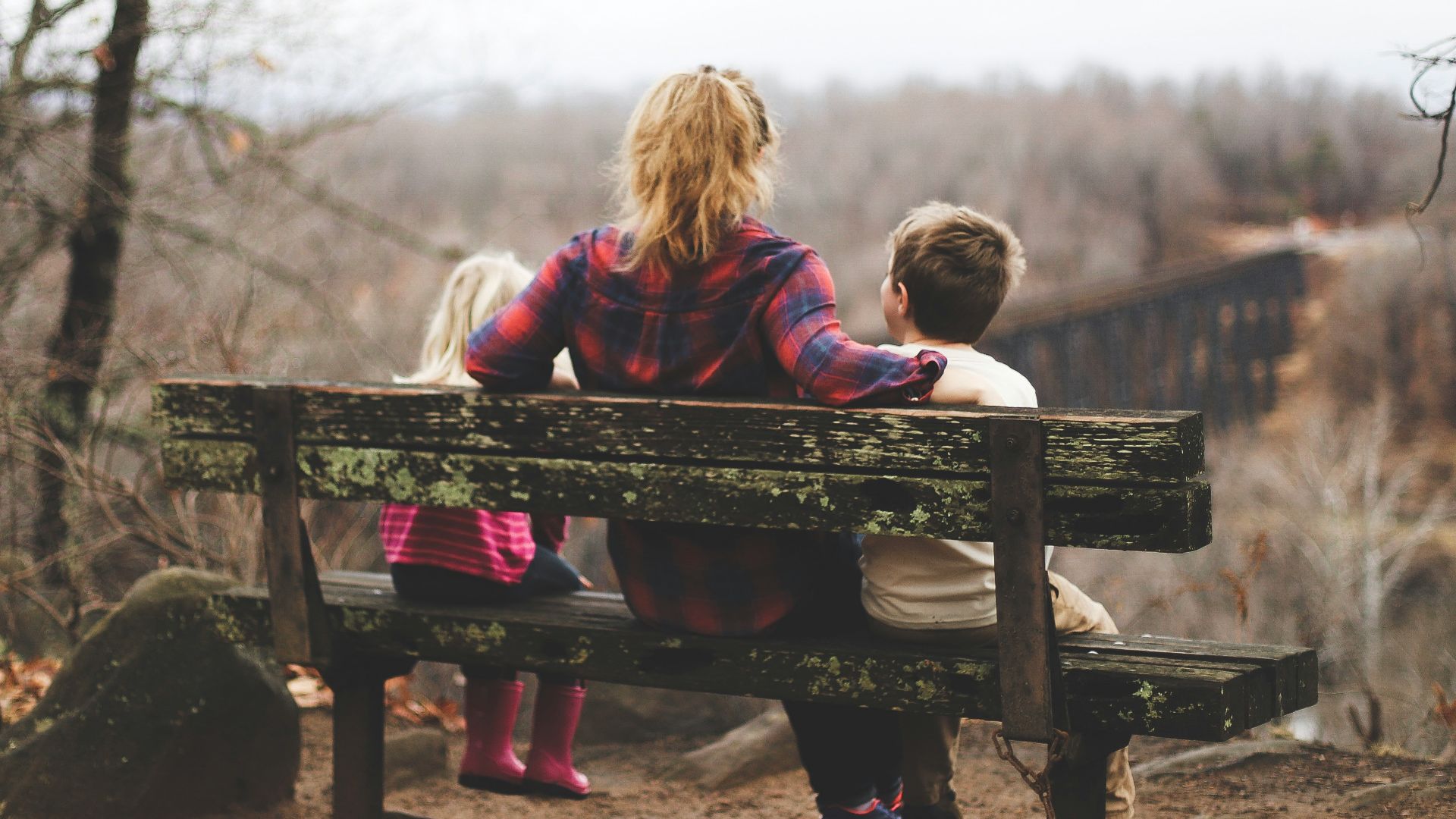woman between two childrens sitting on brown wooden bench during daytime