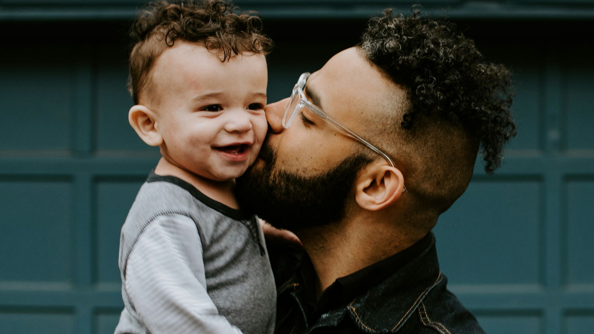 man carrying baby boy and kissing on cheek