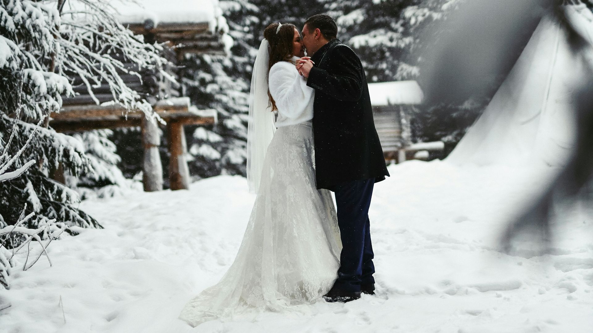a bride and groom kissing in the snow