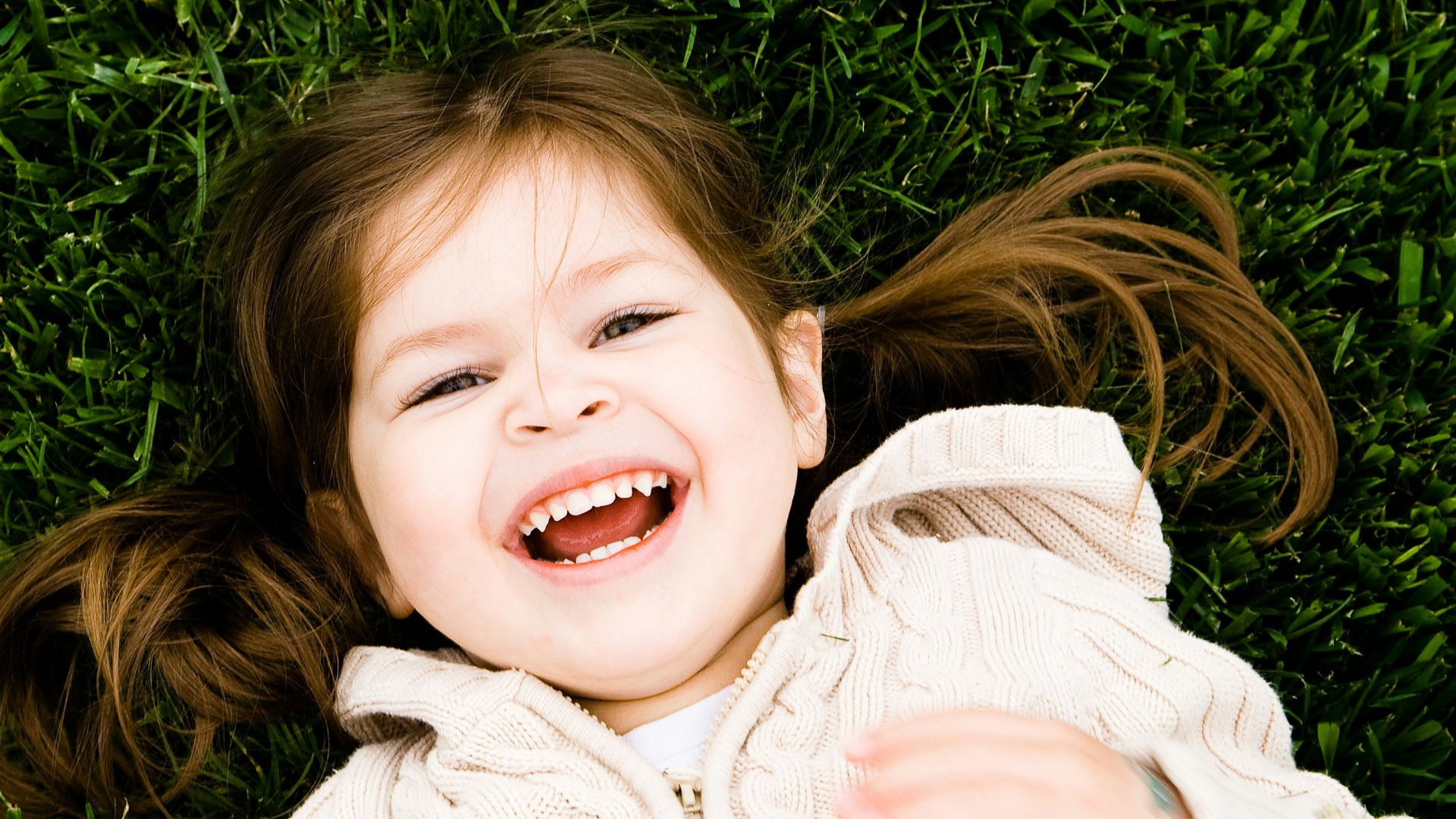 girl smiling while lying on grass field at daytime