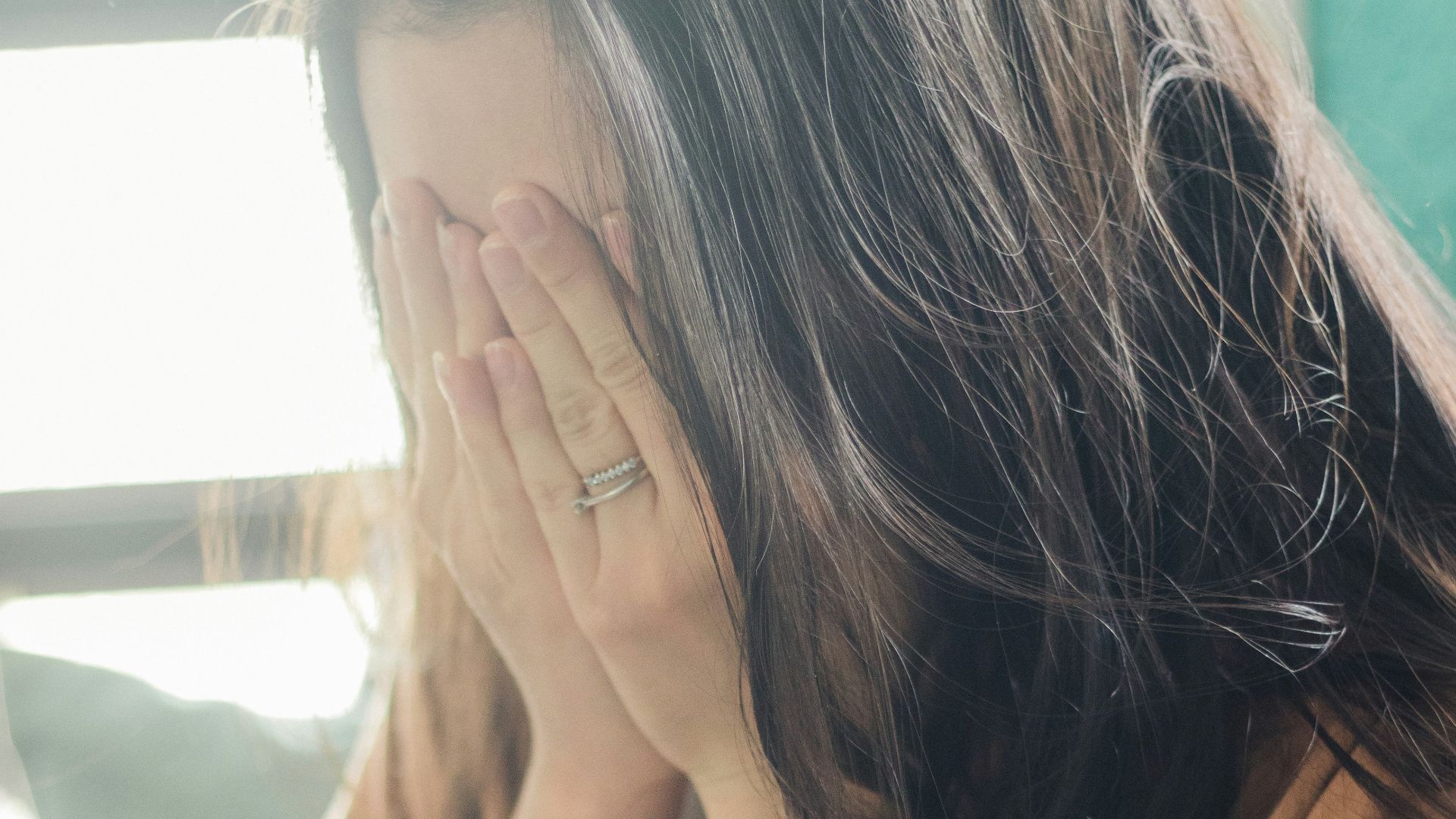 woman in brown shirt covering her face