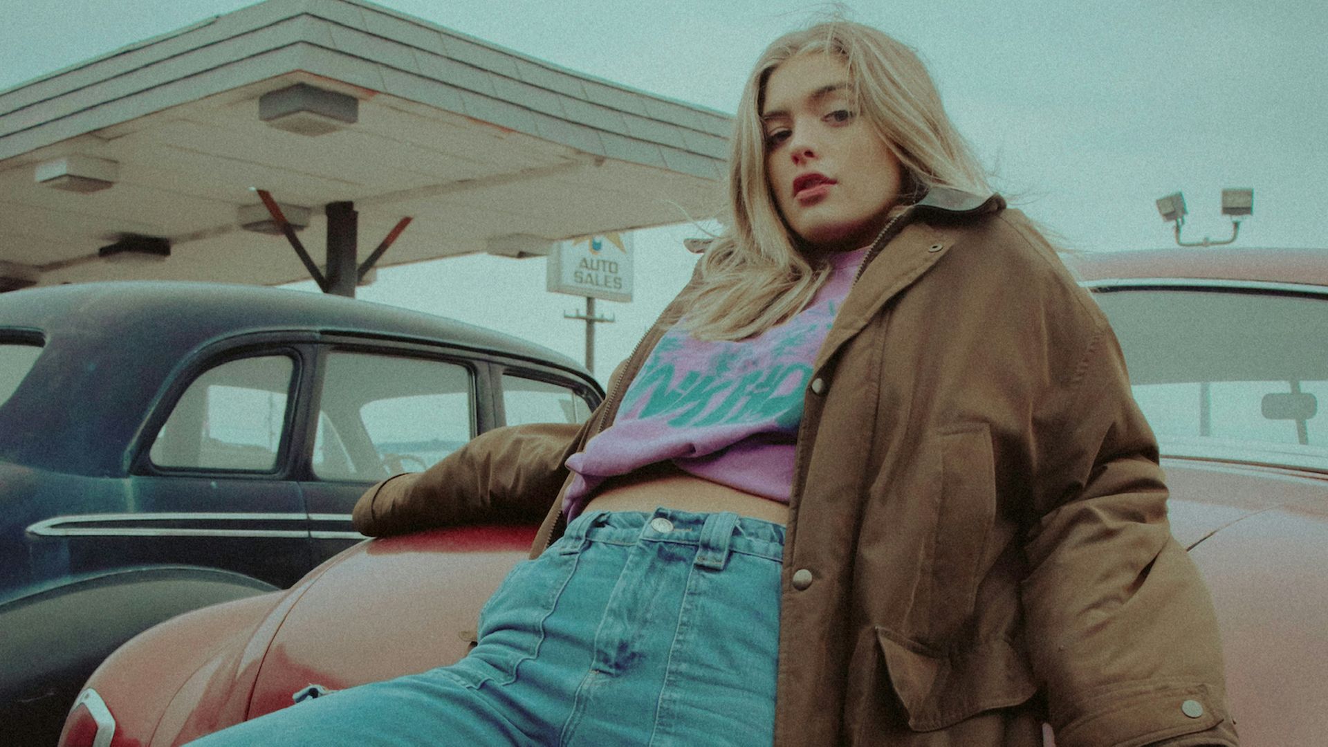 woman in brown jacket and blue denim jeans sitting on red car