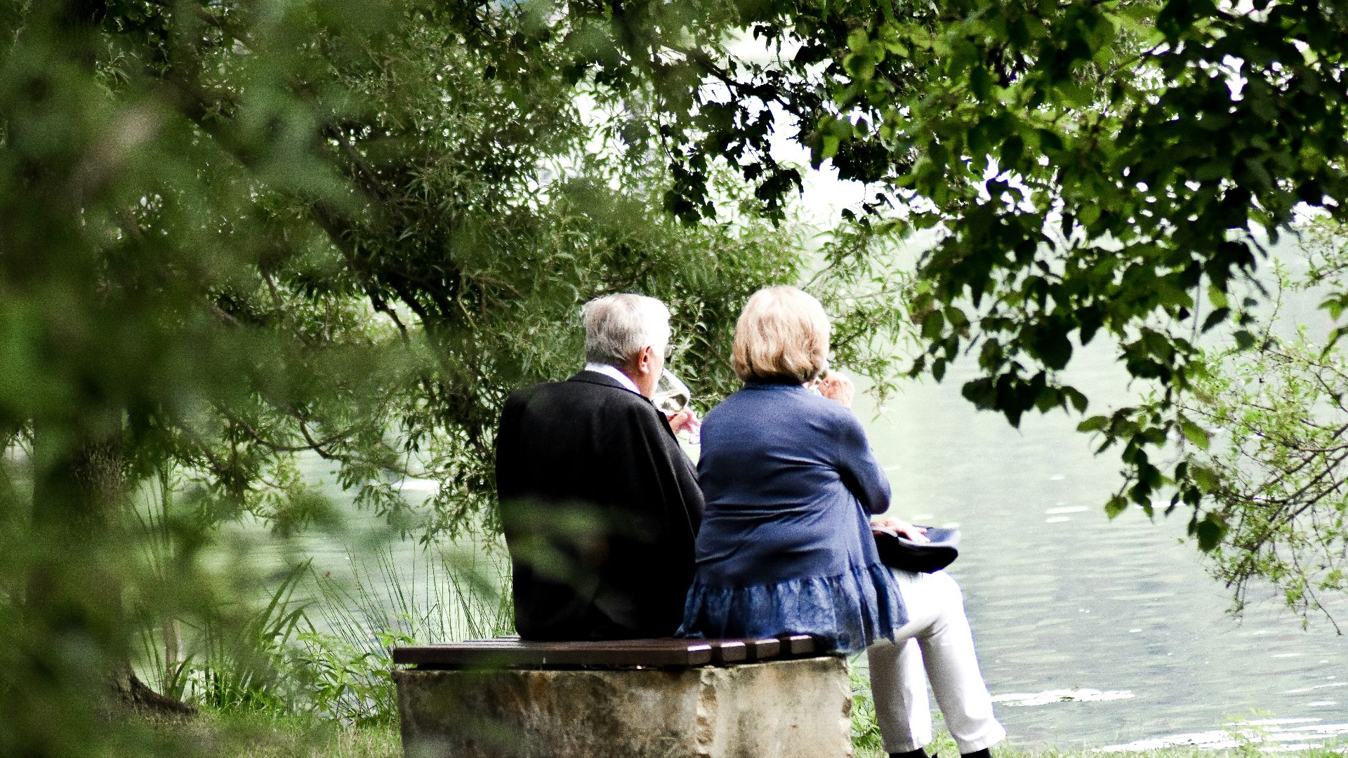 two people sitting on pavement facing on body of water