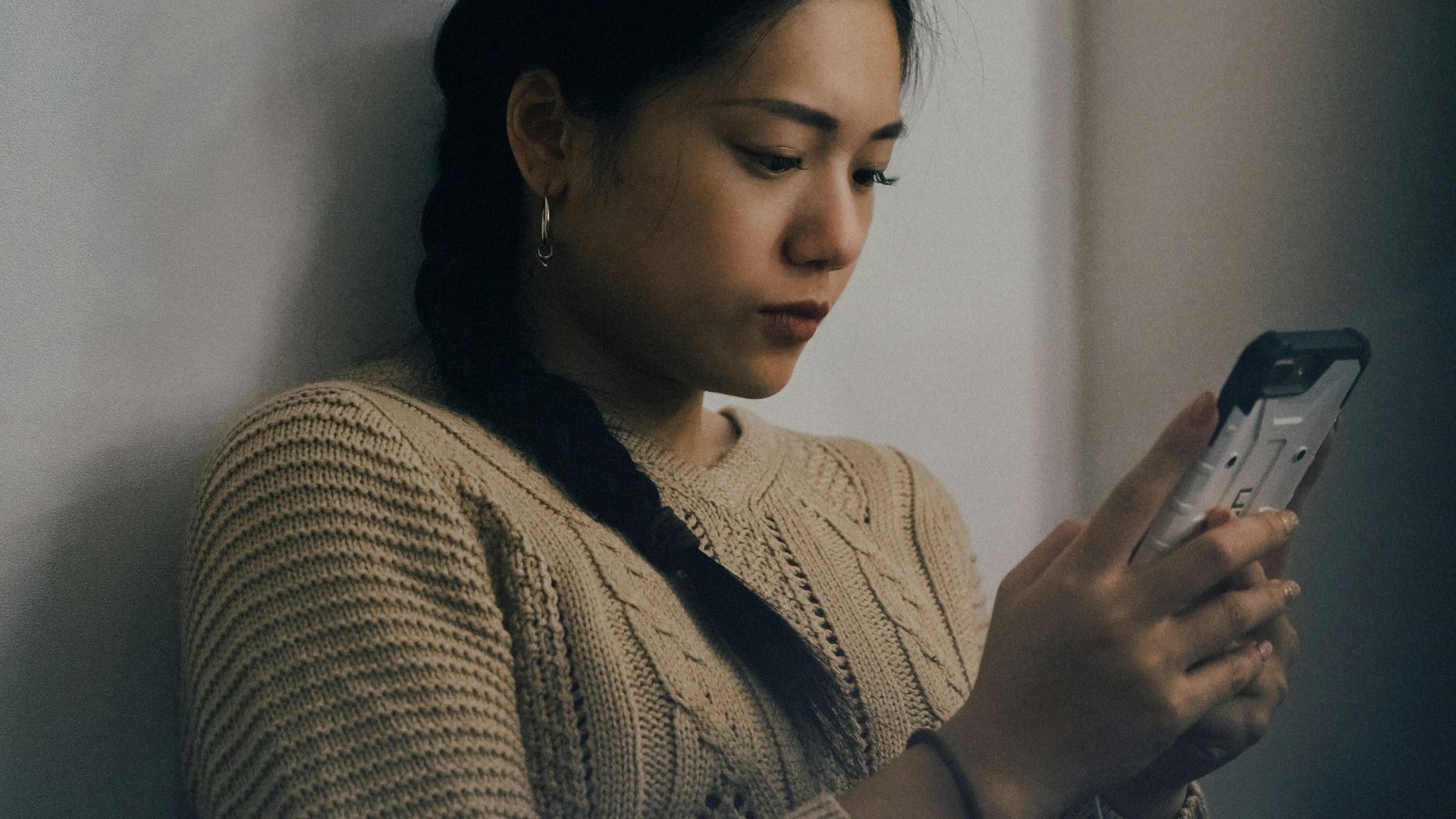 woman leaning back on white wall and using smartphone