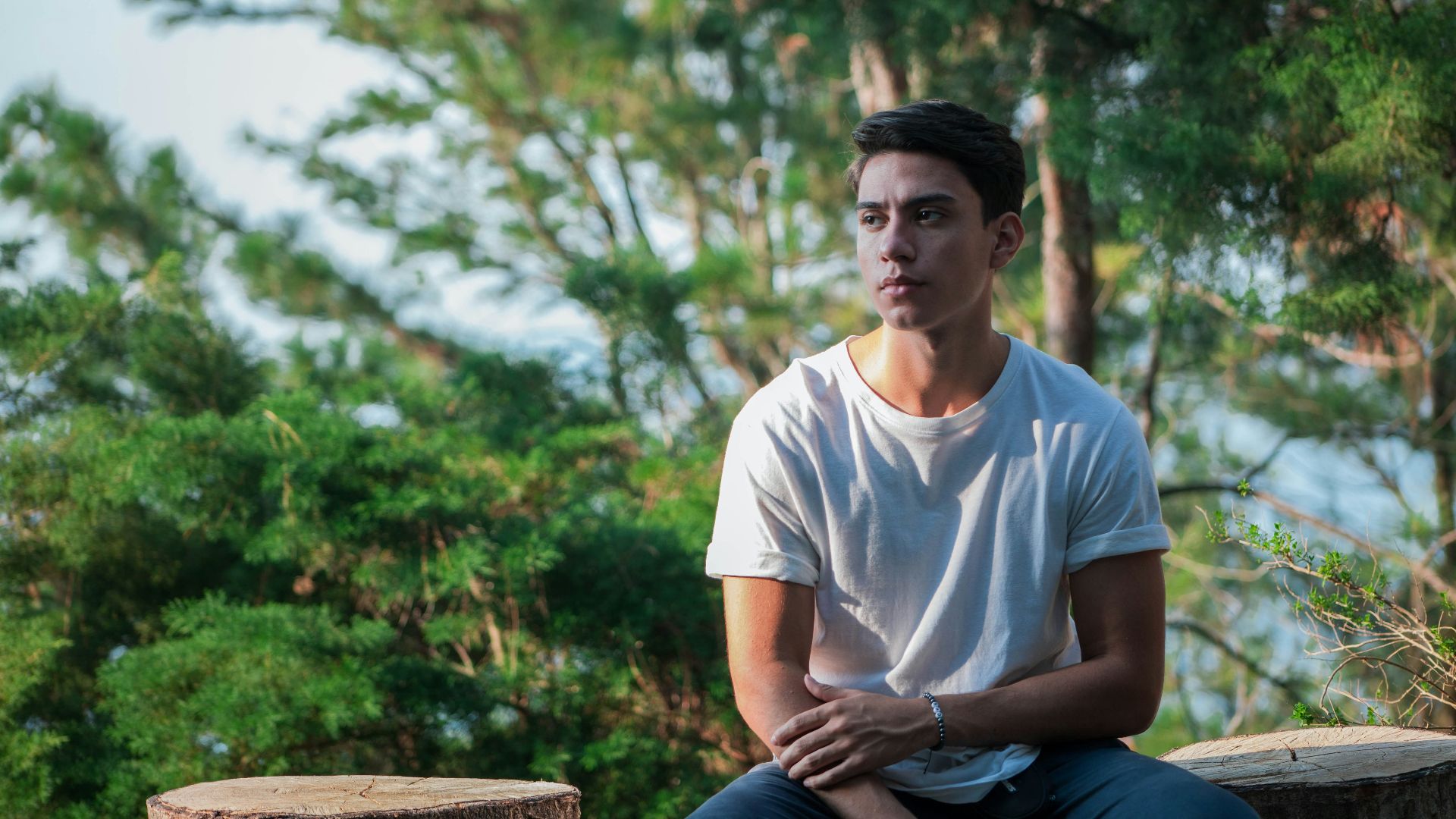 man in white crew neck t-shirt sitting on brown wooden bench during daytime