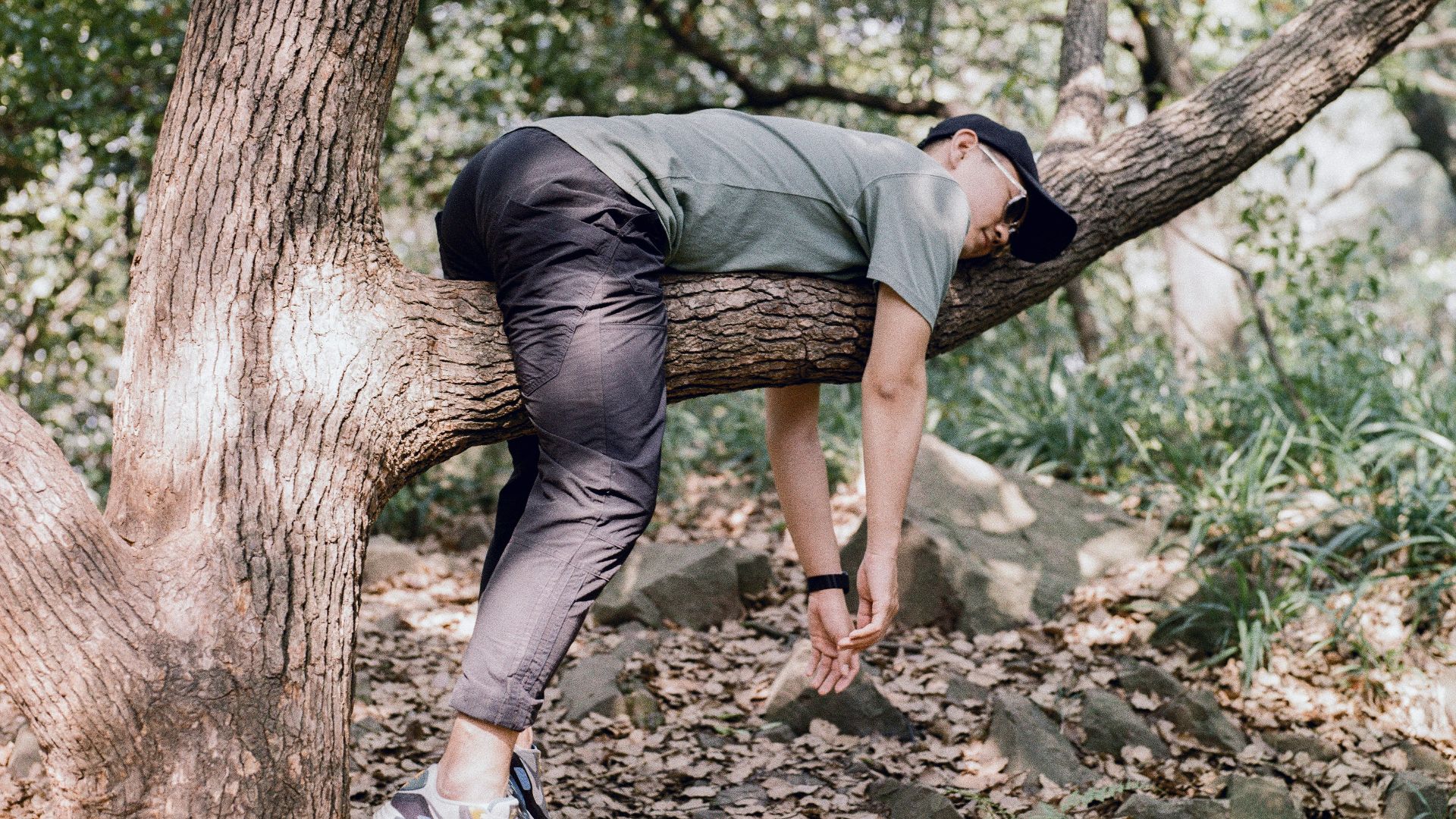 man in black t-shirt and blue denim jeans sitting on tree branch
