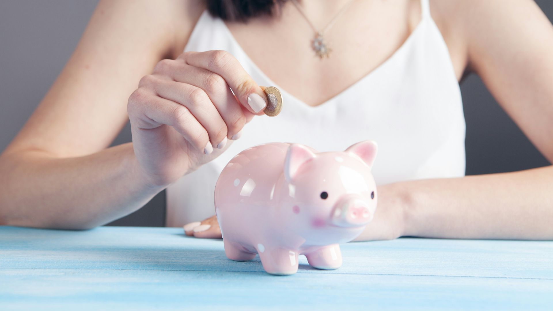 woman in white tank top holding pink pig figurine