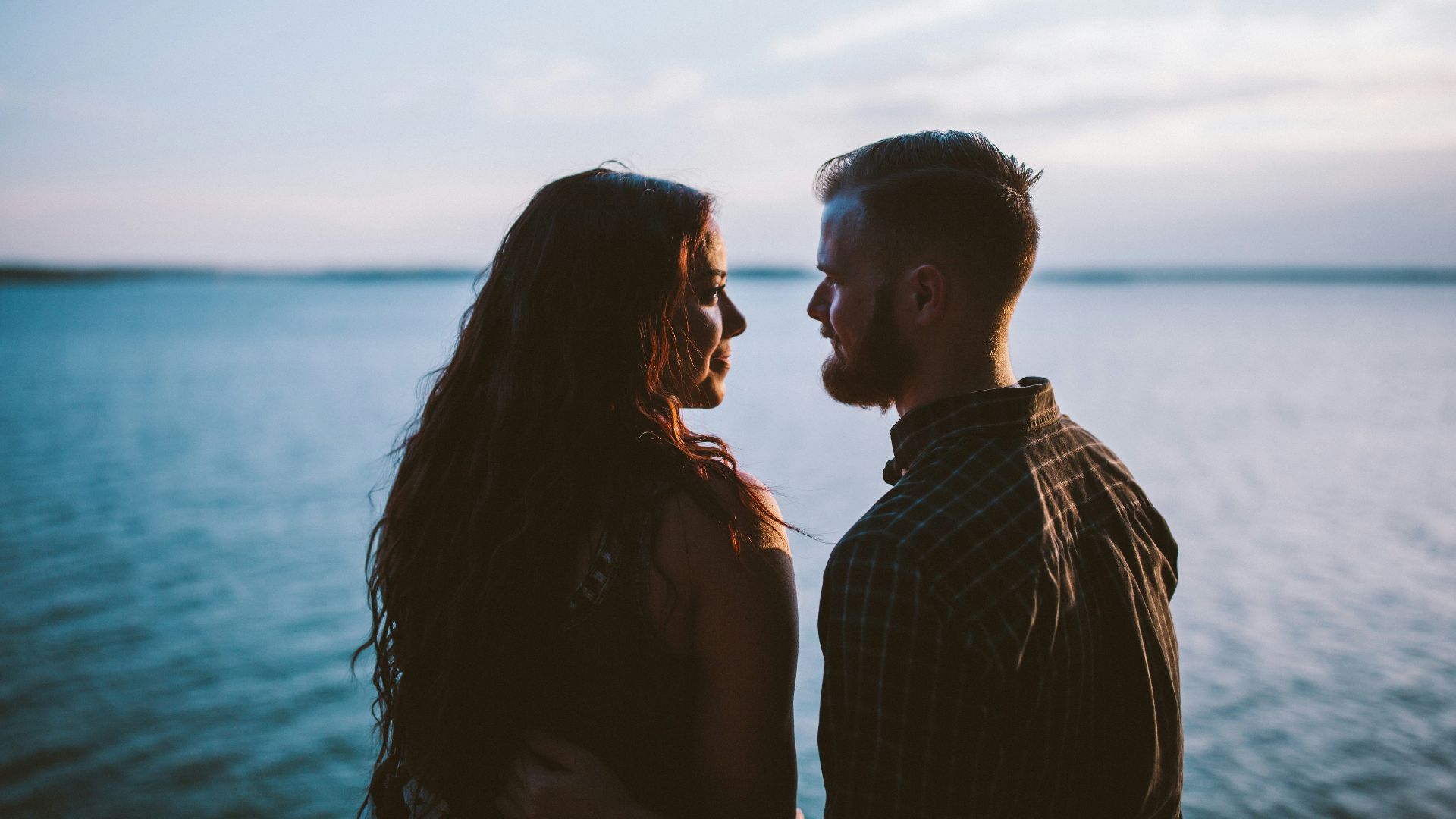man and woman standing while looking each other near body of water