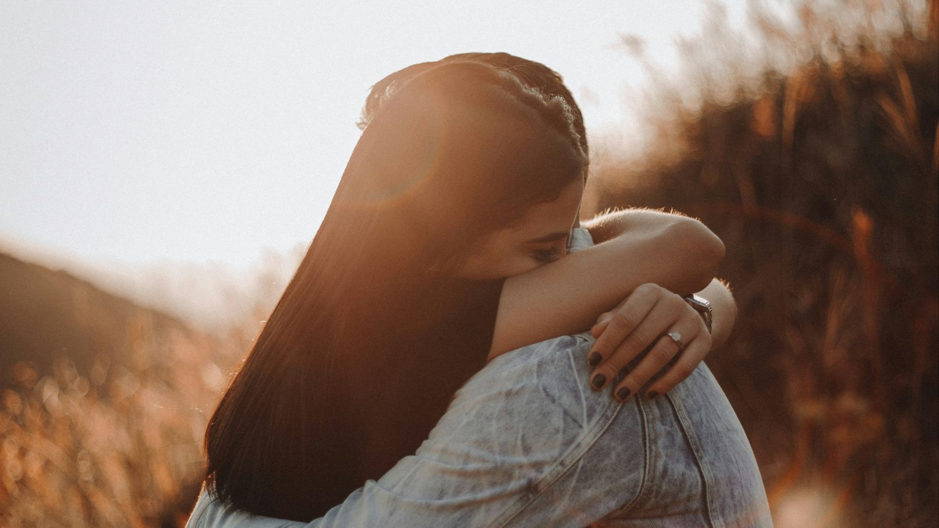 woman in black long sleeve shirt and blue denim jeans covering her face with her hand