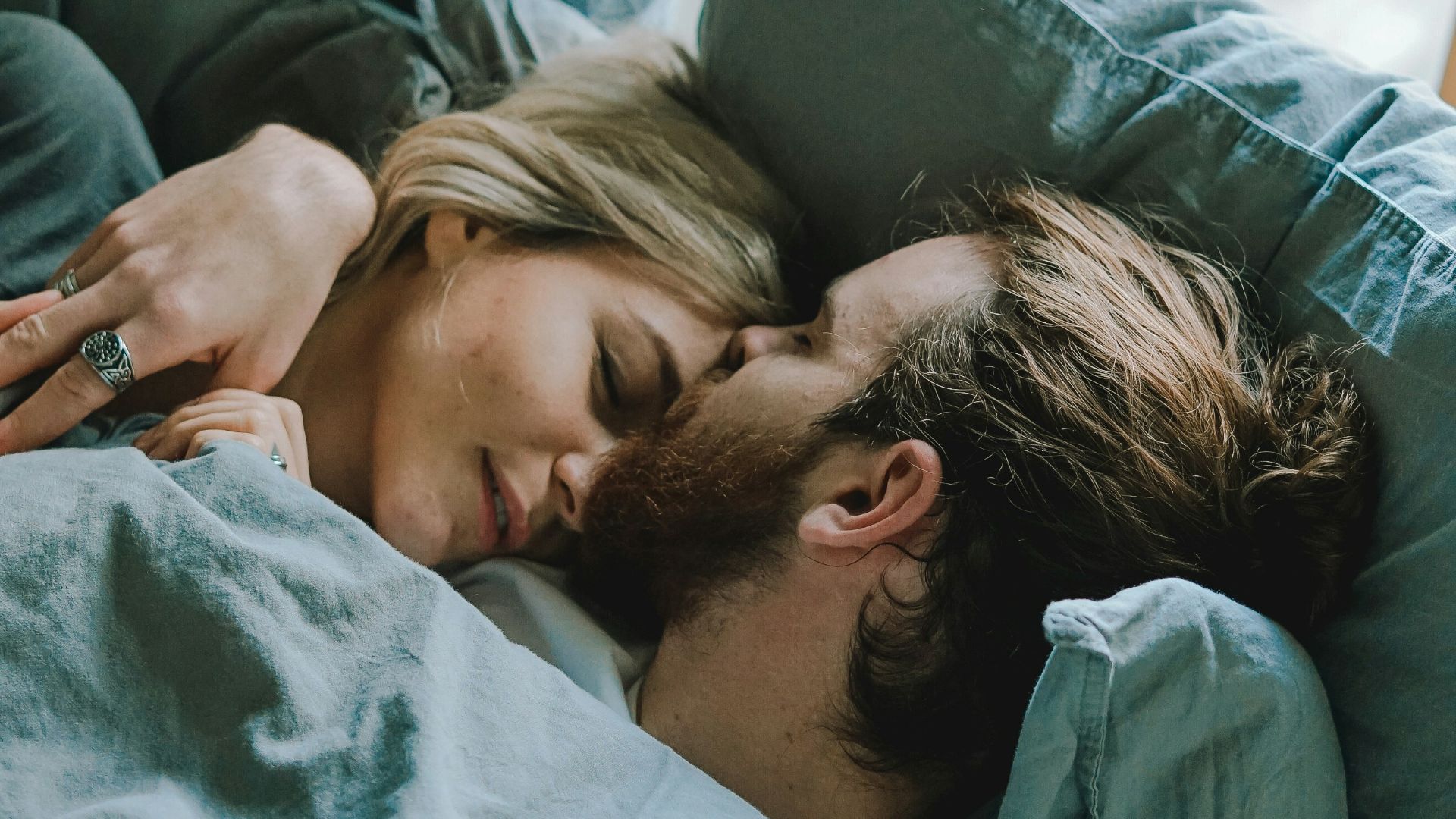 man kissing woman's forehead while lying on bed