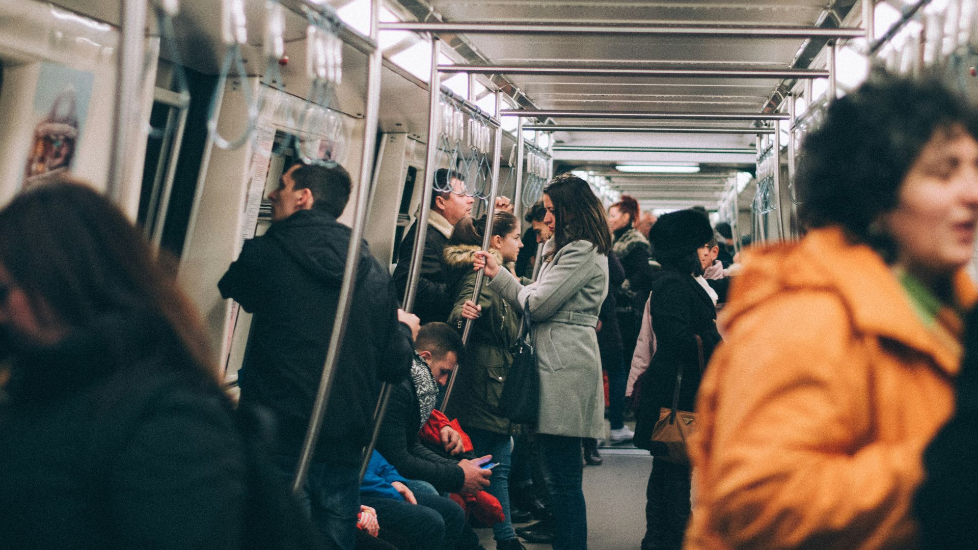 woman standing inside train surrounded by people