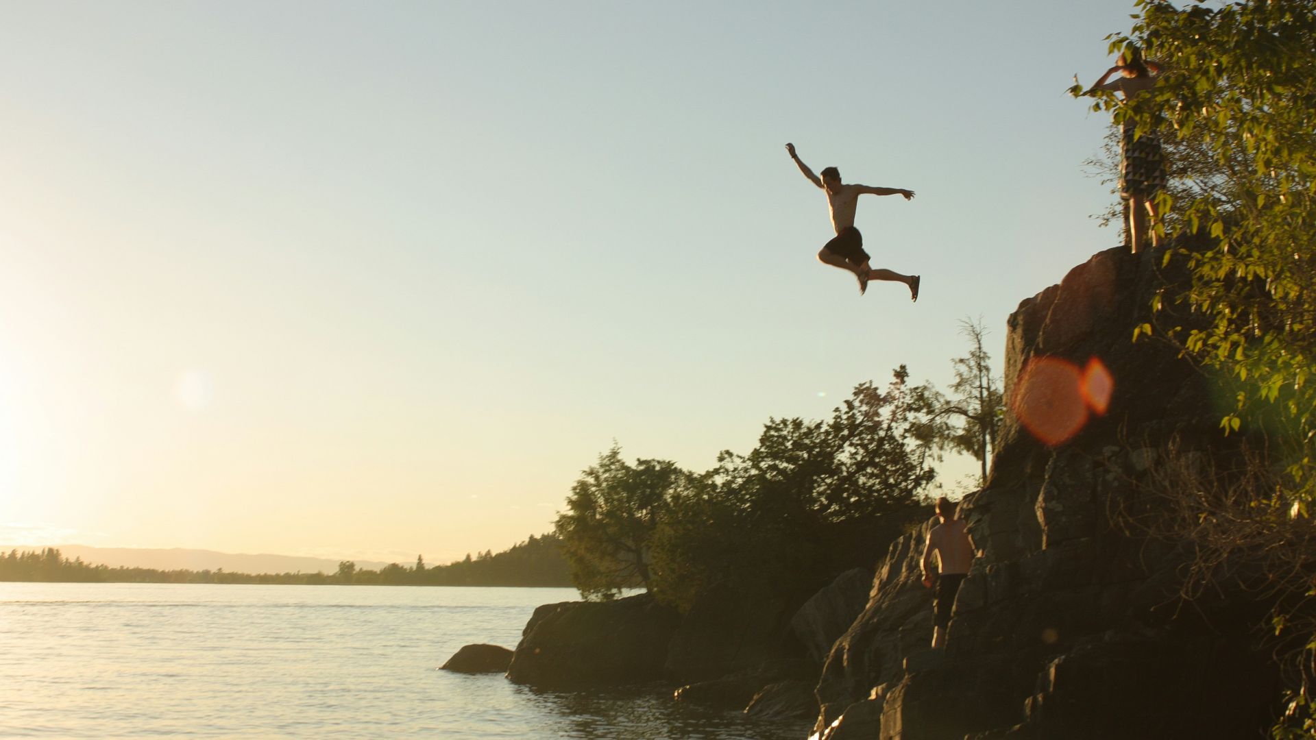 person diving from cliff to body of water during sunset