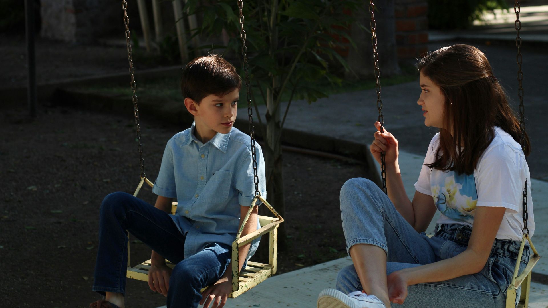 boy in blue long sleeve shirt sitting on swing during daytime