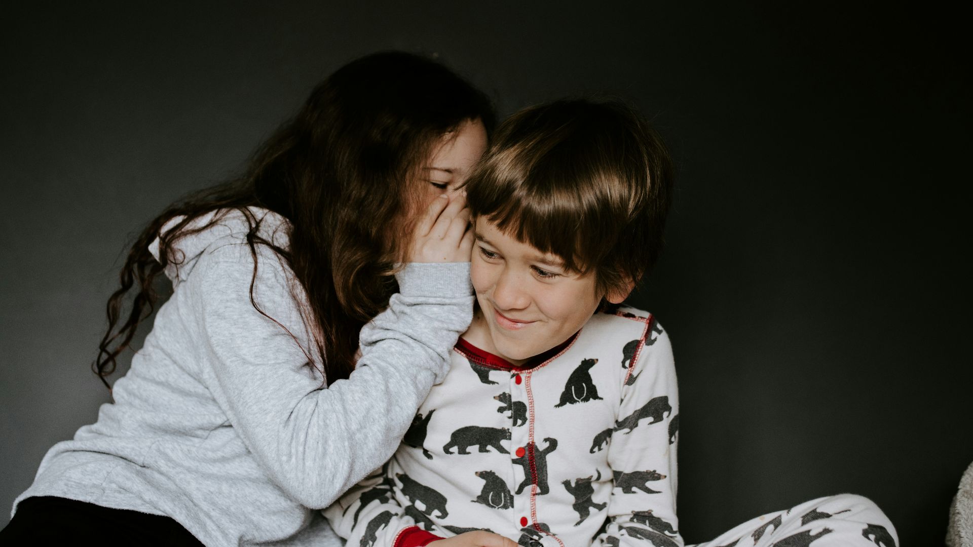 girl in gray jacket whispering on boy's right ear