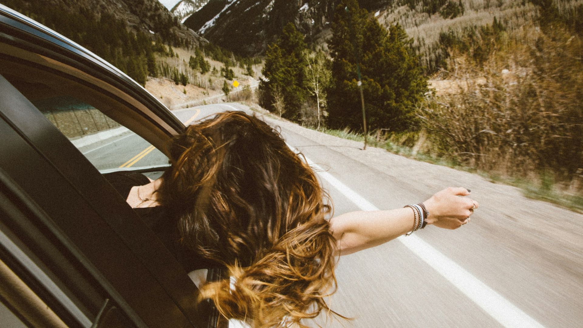 woman riding on vehicle putting her head and right arm outside the window while travelling the road