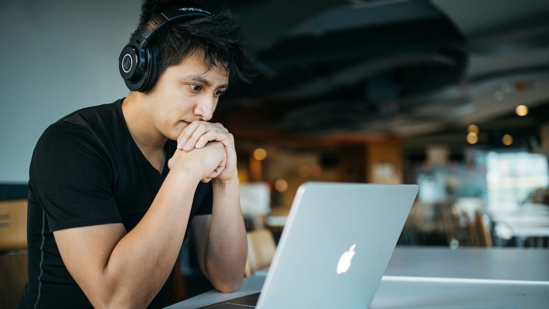 man wearing headphones while sitting on chair in front of MacBook