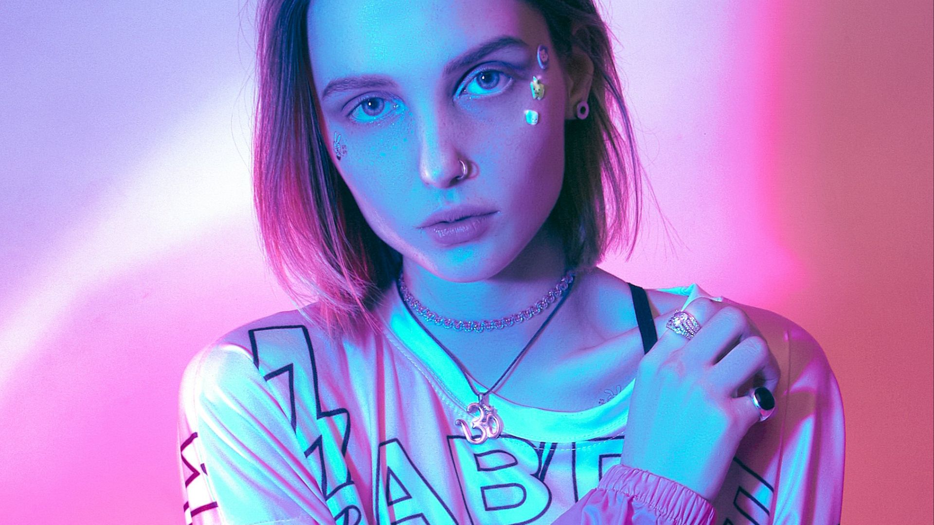 woman in white and pink shirt near white wall with necklace