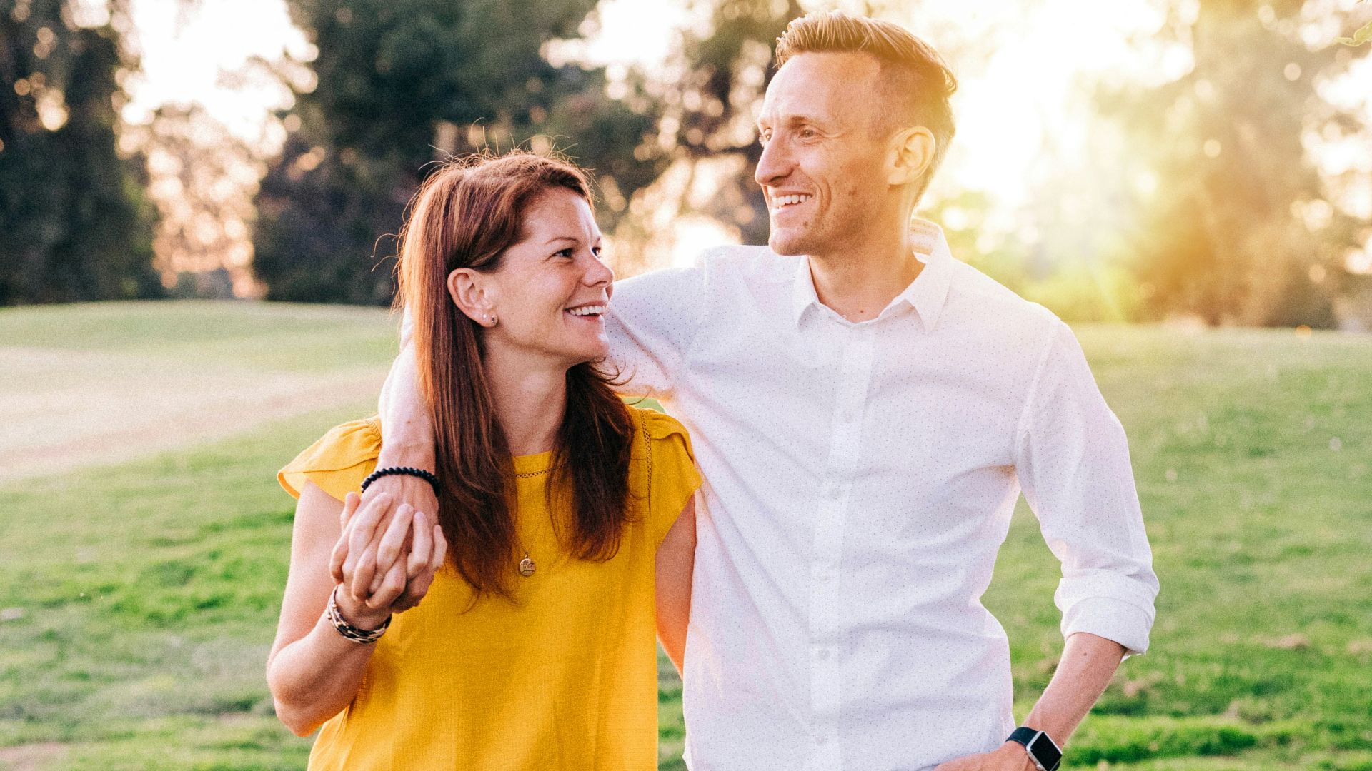 man in white dress shirt and woman in orange long sleeve shirt standing on green grass