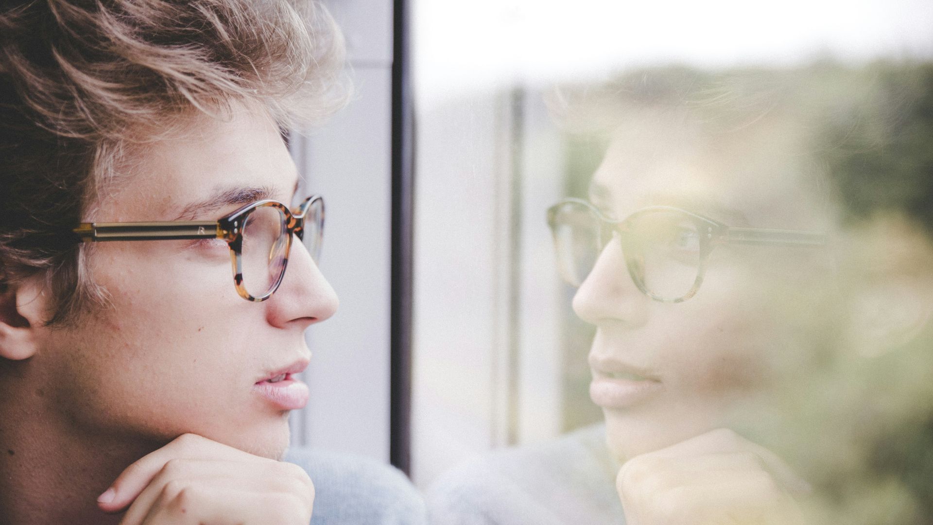 a man wearing glasses looking out a window