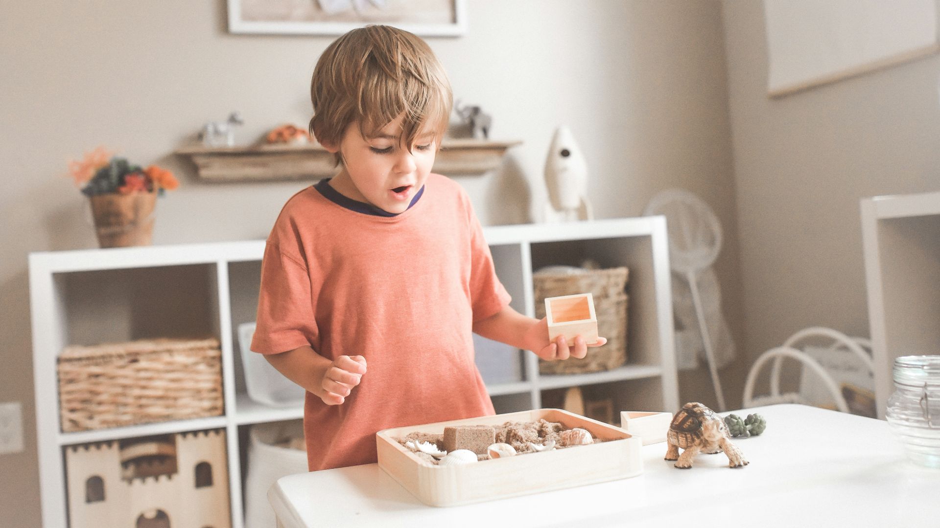 boy in orange crew neck t-shirt standing in front of white wooden table with cupcakes
