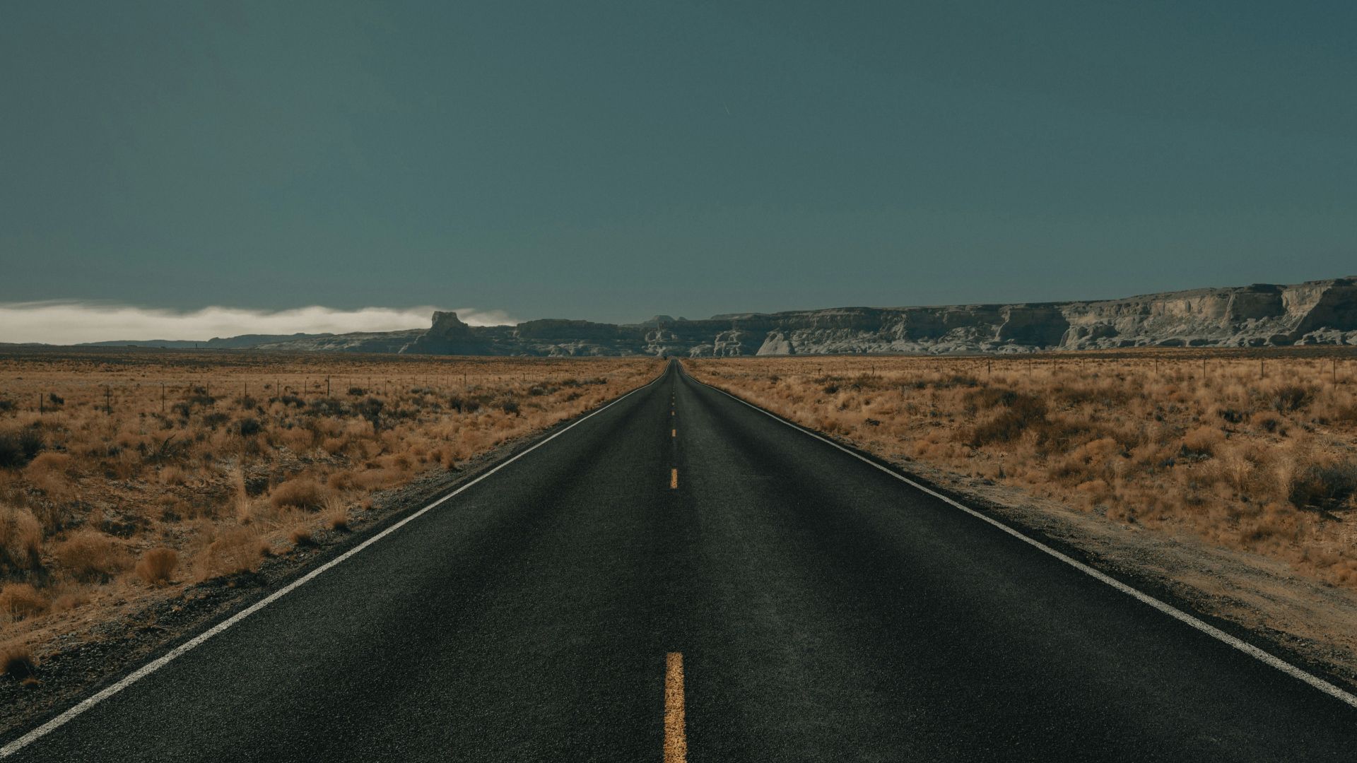 black asphalt road between brown grass field under blue sky during daytime