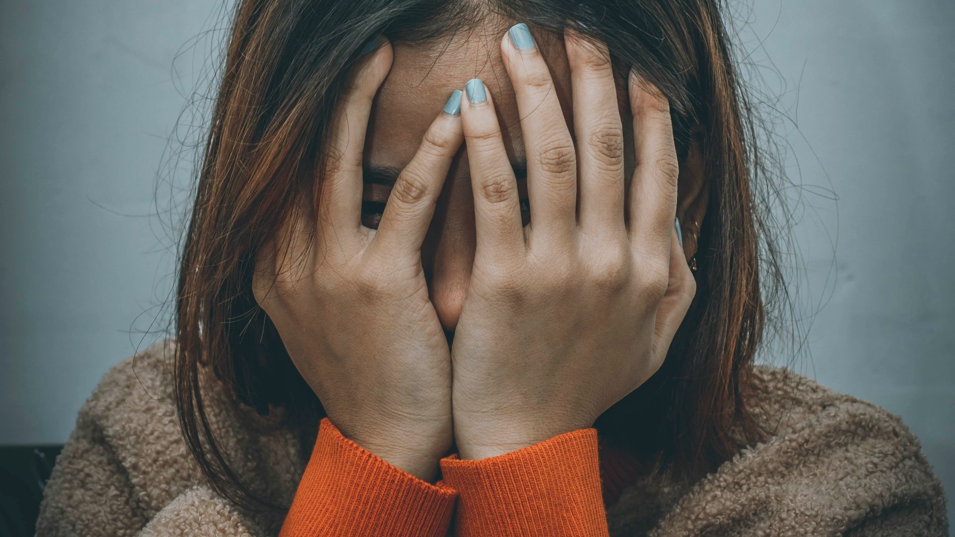 woman in brown sweater covering her face with her hand