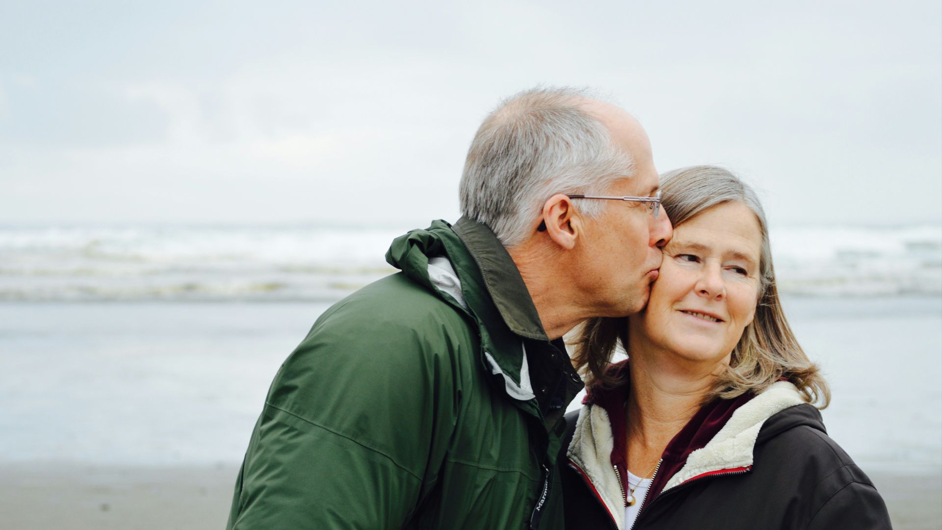 man kissing woman on check beside body of water